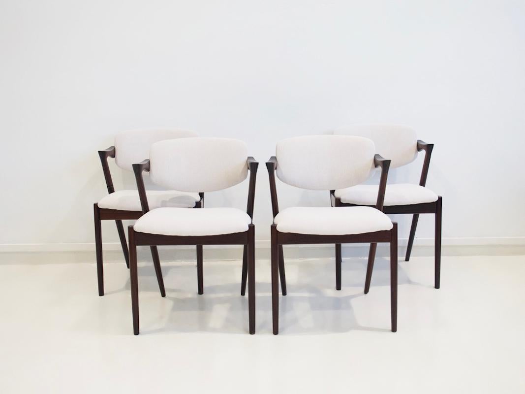 Four stained oak chairs with tilting back reupholstered in off white fabric. Designed by Kai Kristiansen, manufactured by Schou Andersen Møbelfabrik. Minor scratches and marks in wood.