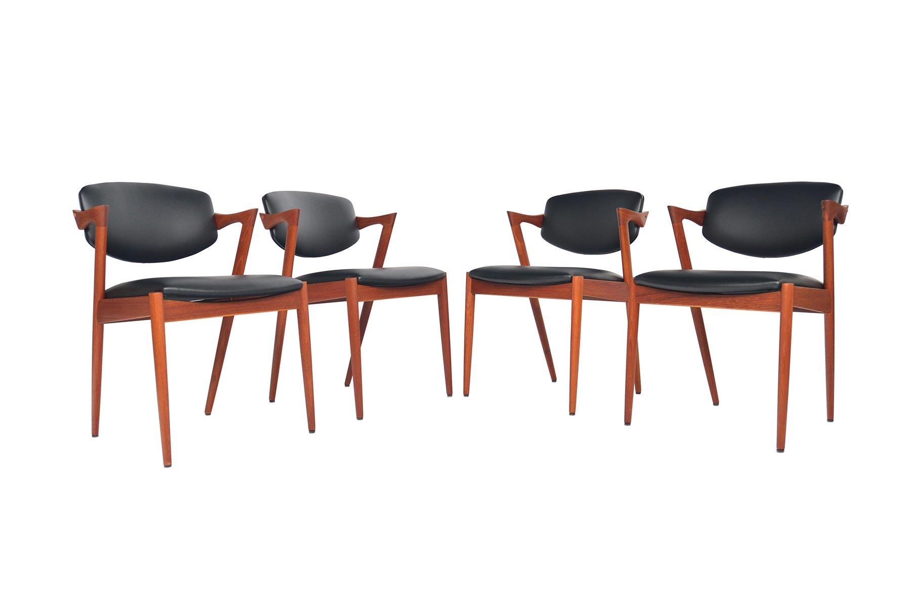 This incredible set of four Model 42 dining chairs was designed by Kai Kristiansen for Schou Andersen Møbelfabrik in 1957. Crafted in solid teak, these chairs feature a dramatic profile with a sleek armrest that extends into a canted back leg.