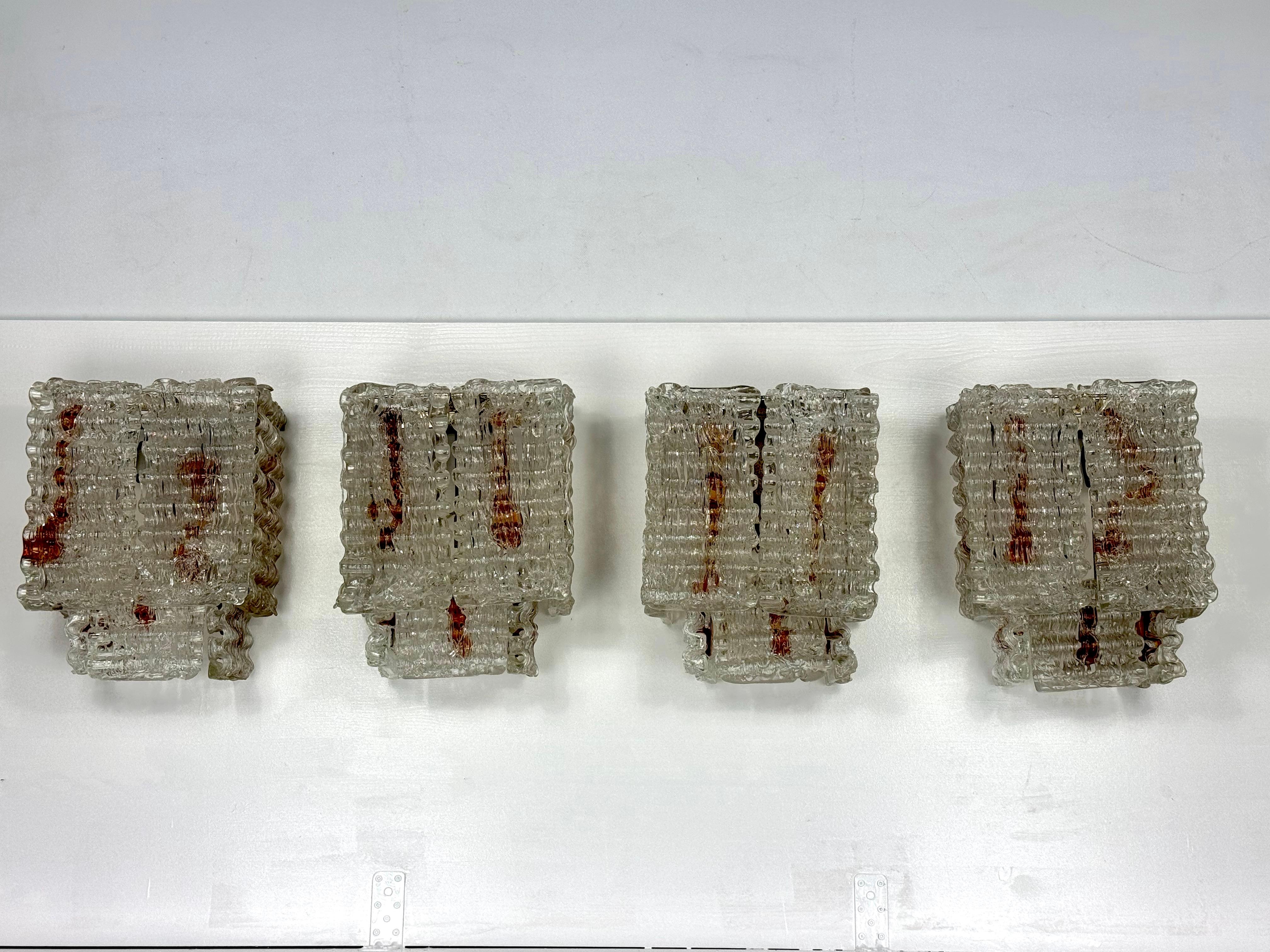 Juego de cuatro apliques de elementos de cristal de murano en transparente y ámbar. Muy buen estado vintage sin grietas ni astillas. Restos de oxidación en los soportes metálicos. Funcionamiento completo con la norma de la UE, adaptable bajo demanda