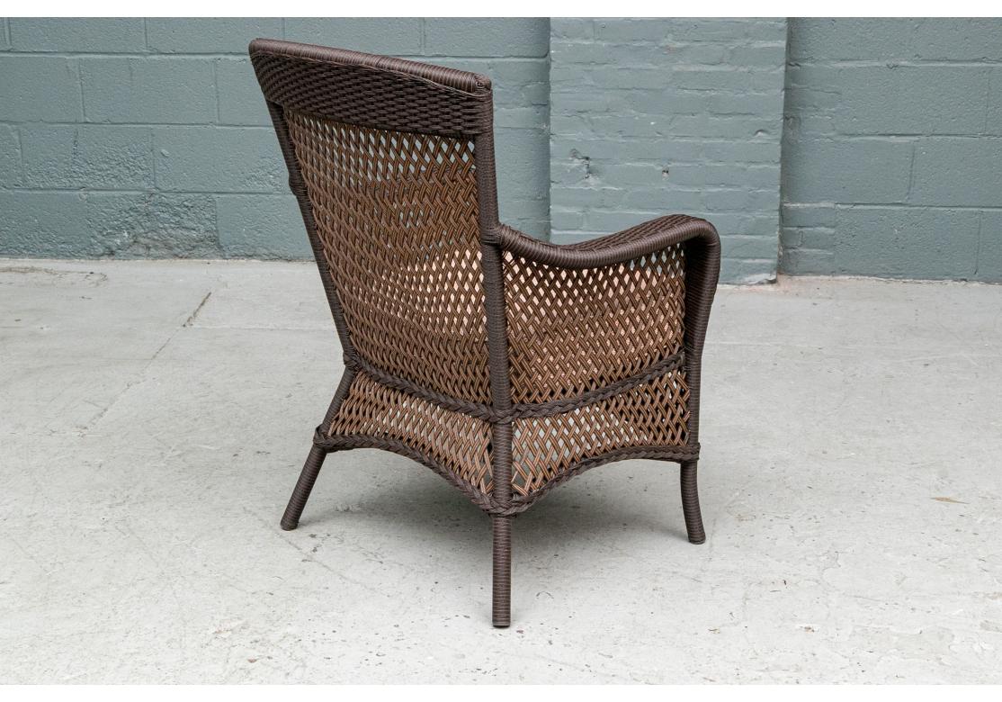 Well- crafted comfortable woven vinyl wicker armchairs in dark brown frames with a brown two-tone open lattice weave on the backs, sides and skirt rails.  With sloping backs and raised on splayed legs. Along with quality peach tone tweed fabric