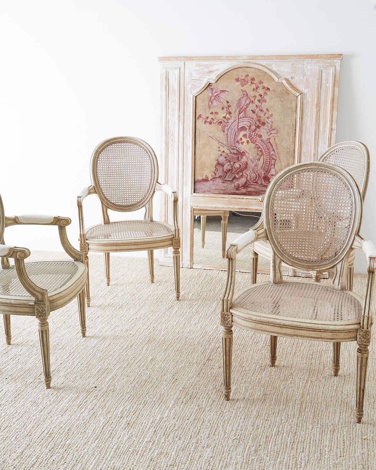 Elegant set of four French Louis XVI style dining chairs of armchairs. Featuring a hand caned seat and back with a lacquered frame in the Gustavian taste. Beautifully carved with round backs and molded arms attached to a bow front seat with