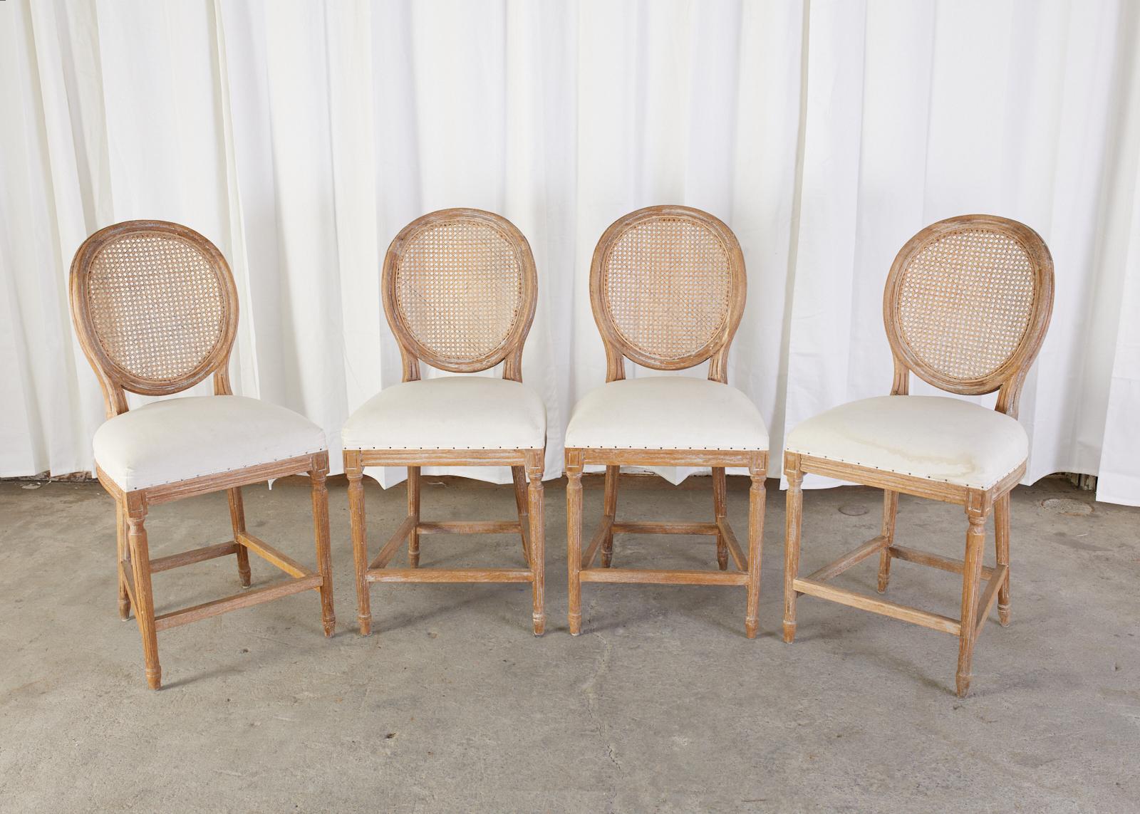 Gorgeous set of four oak counter height bar stools with round cane backs. Made in the grand French Louis XVI style featuring an intentionally age, distressed, pickled, or bleached finish on the oak. The wood also has a lightly cerused patina to