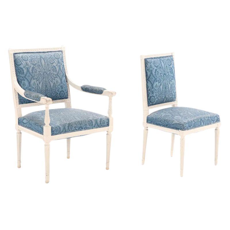 A set of four Louis XVI style painted and upholstered dining chairs, circa 1930.  Two arm chairs and two side chairs with carved and painted white square back frames and fluted legs.  Chairs are upholstered with blue damask fabric in a timeless and