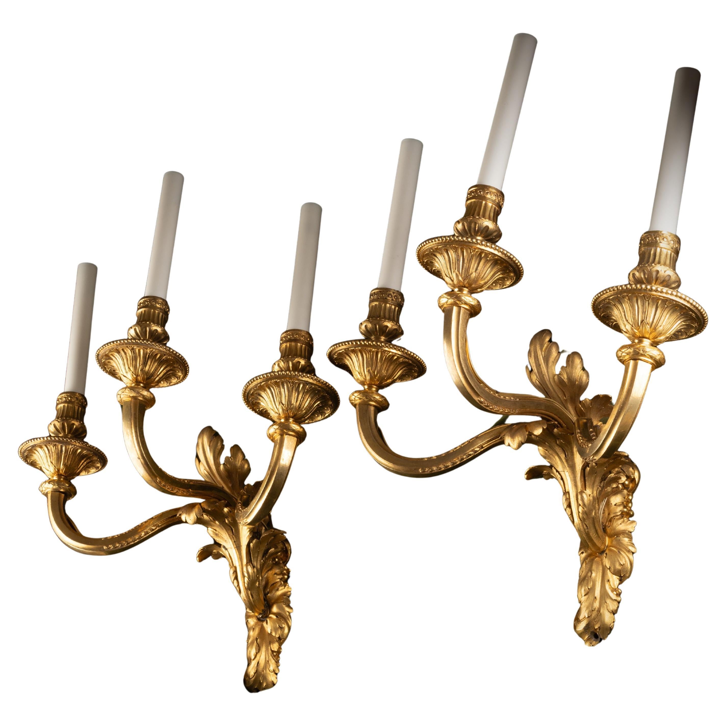 Juego de cuatro apliques de pared de tres luces, estilo Luis XVI, en bronce dorado