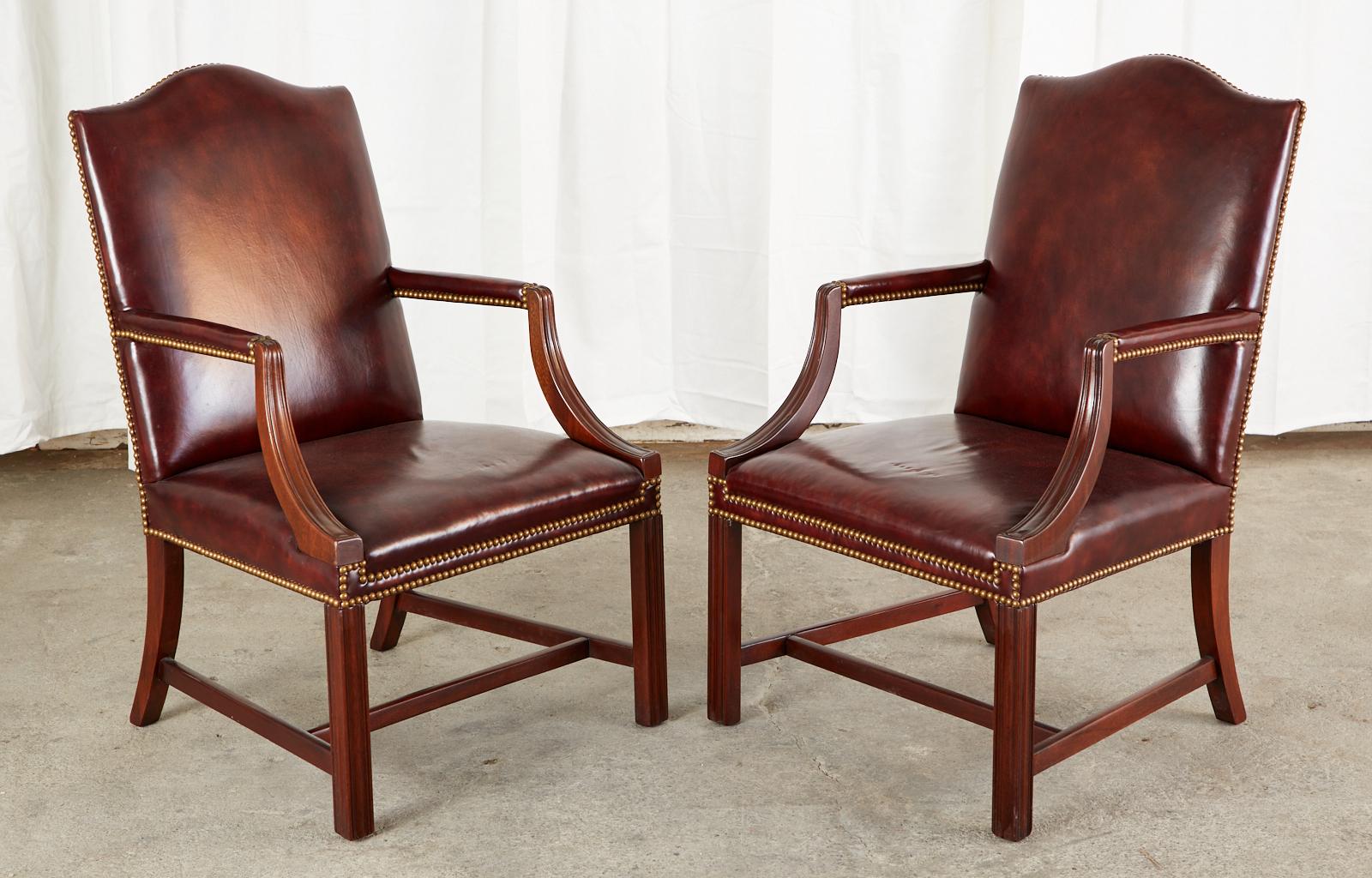 Handsome set of four mahogany and leather library armchairs made in the Georgian Gainsborough style. The stately chairs feature a distinctive mahogany frame with gracefully curved arms supporting padded armrests. The seat has a classic flatback with