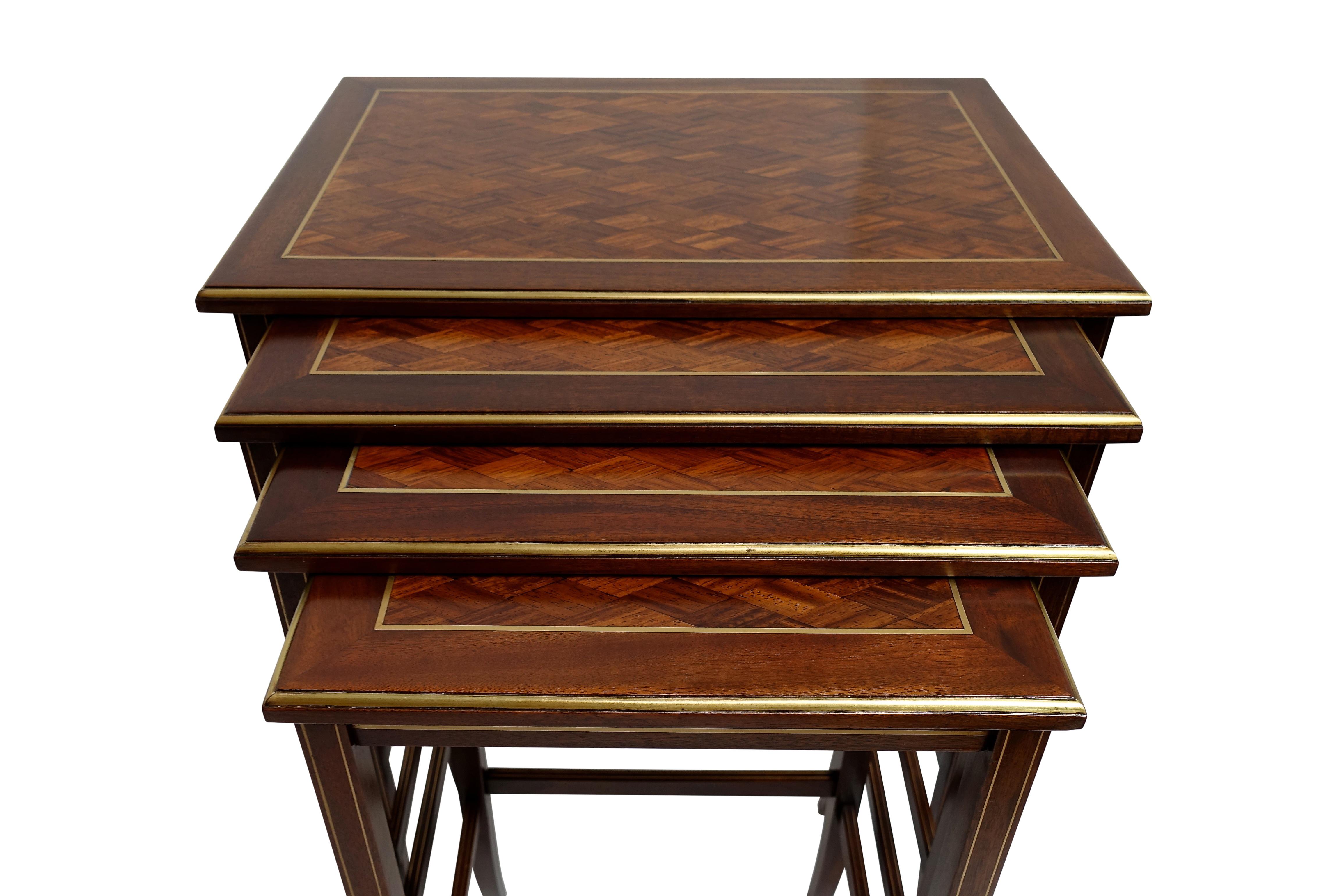 An attractive set of four mahogany nesting tables with a parquetry tumbling block pattern on the top surface, and having brass inlay around the top, on the legs and the stretcher bar, American, mid-20th century.