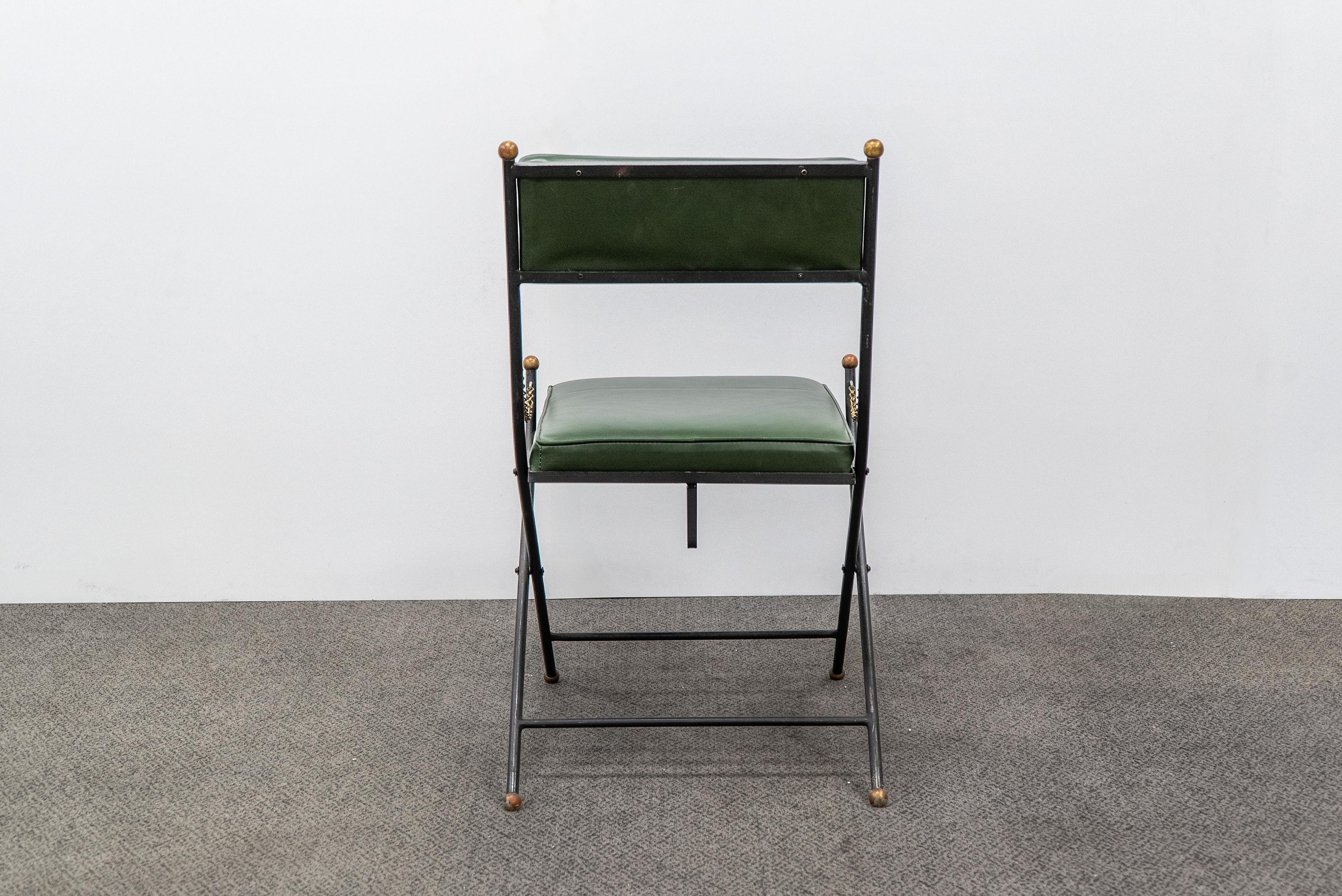 Set of four (4) campaign folding chairs in the style of Maison Jansen upholstered in green leather. They feature brass metal embellishments on the frames and chain details which hang on either side. These chairs can be folded and stowed away