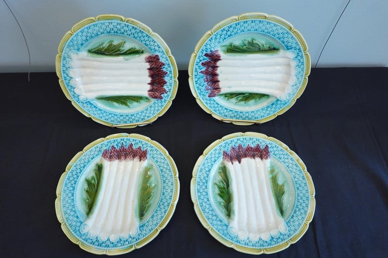 Set of four colorful French majolica asparagus plates attributed to Orchies. Each plate features six amethyst-colored molded asparagus spears resting on a leaf on a plate with turquoise colored basketweave surround and tan edges. Plates have