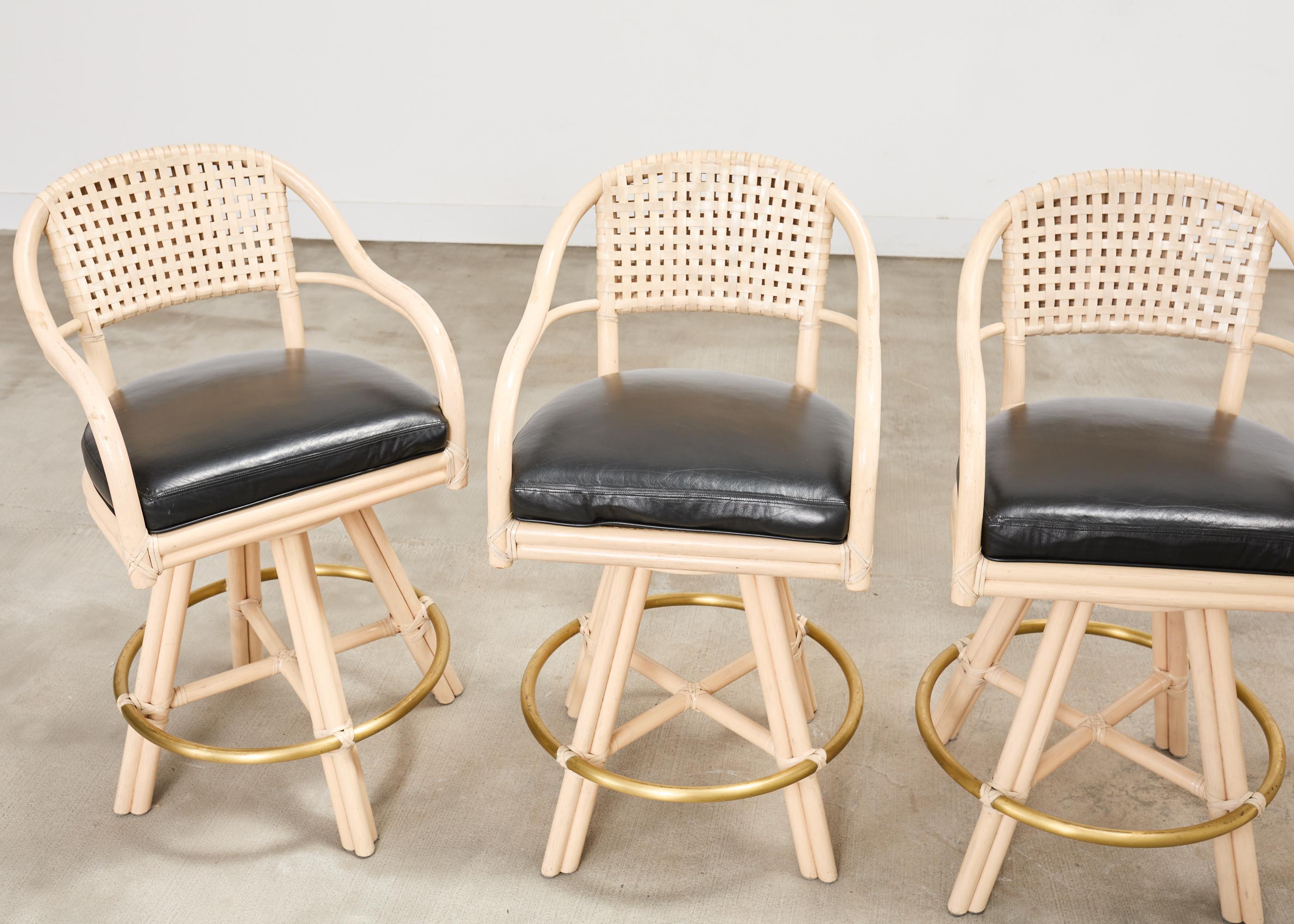 Set moderno e organico di quattro sgabelli da bar in rattan laccato con sedili girevoli. Gli sgabelli sono caratterizzati da uno schienale in rattan curvato e graziosamente ricurvo, con lacci in pelle rawhide in un design geometrico a reticolo. La
