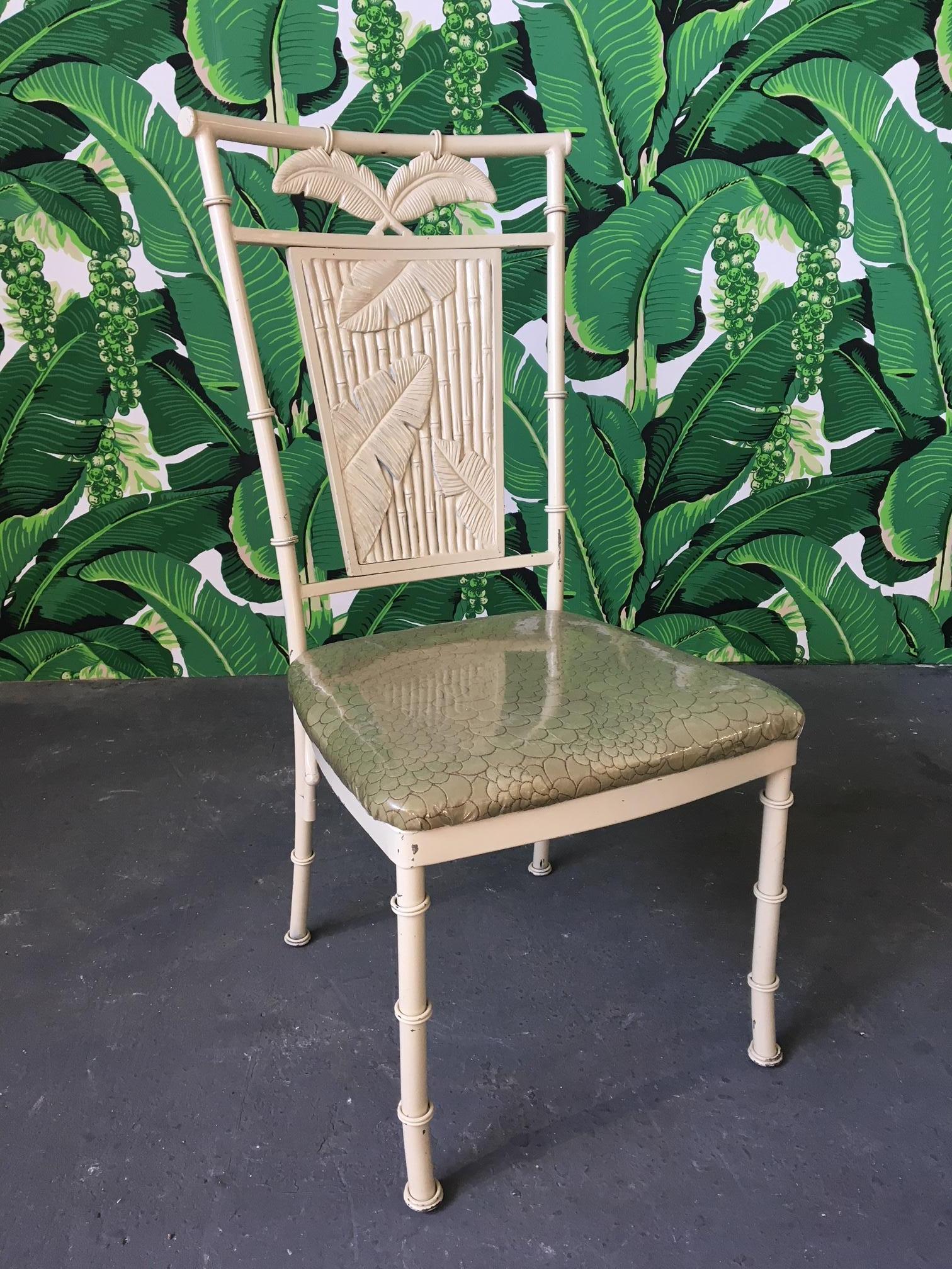 Set of four metal faux bamboo dining chairs with palm motif backs. Upholstered in green fabric with clear vinyl covering. Very heavy and solid with a steel frame construction. Good vintage condition with chips to finish and minor cracks not