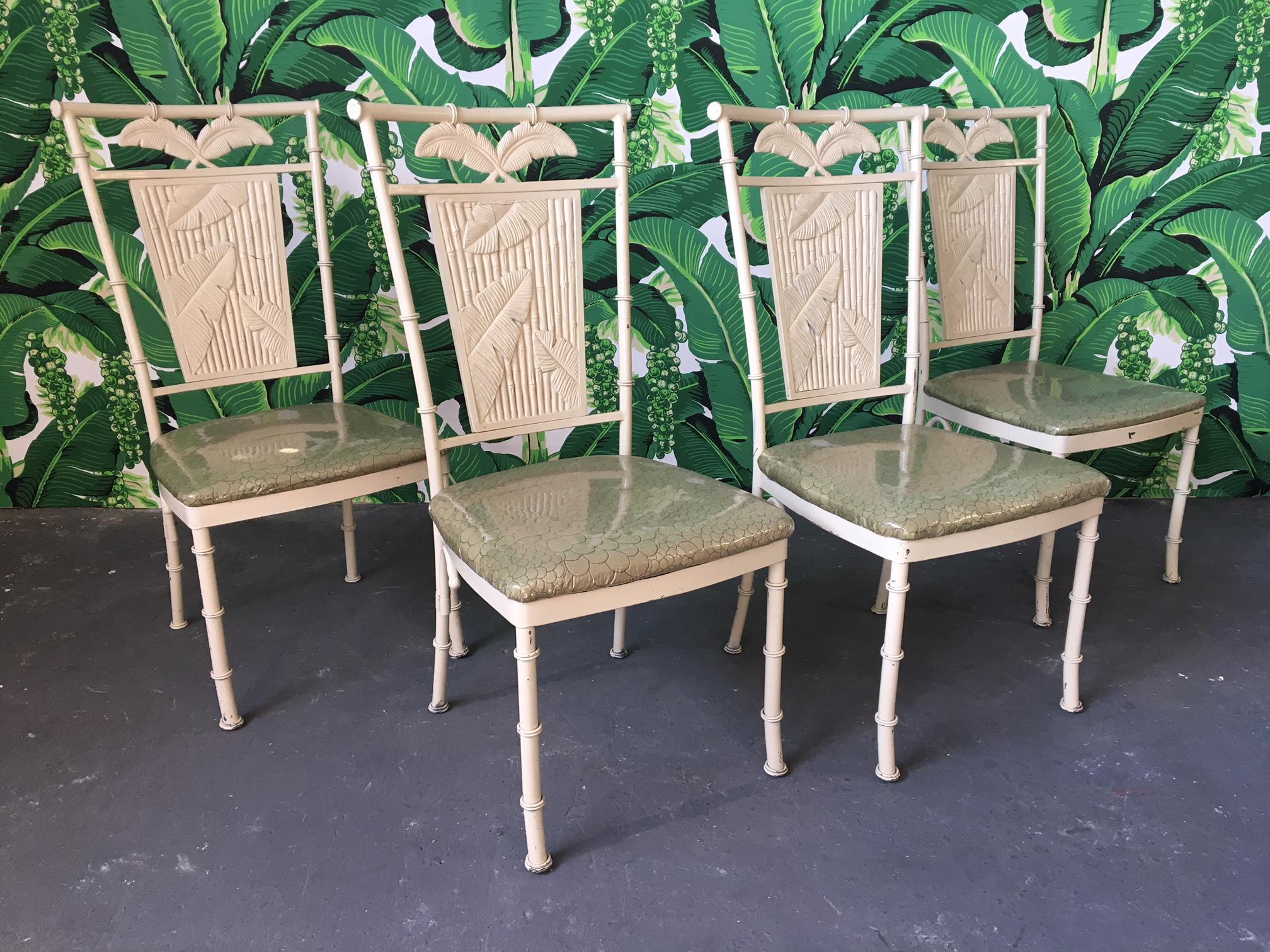 Set of four metal faux bamboo dining chairs with palm motif backs. Upholstered in green fabric with clear vinyl covering. Very heavy and solid with a steel frame construction. Good vintage condition with chips to finish and upholstery in near
