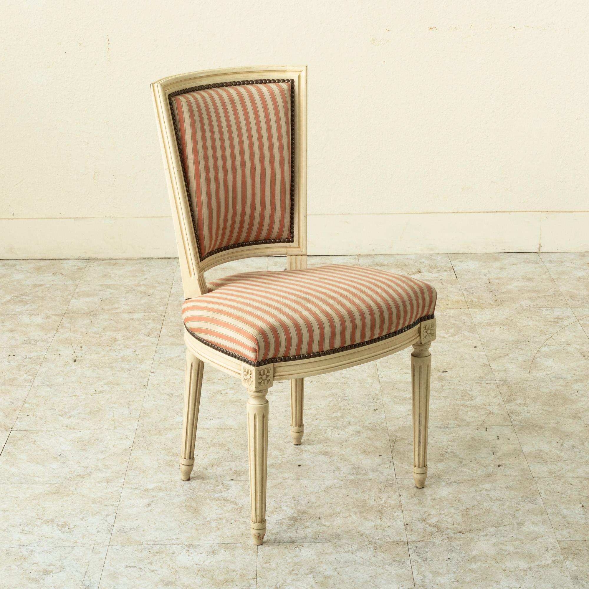 Cet ensemble de quatre chaises de salle à manger ou chaises d'appoint françaises peintes du milieu du siècle est de style Louis XVI classique. Les articulations de la matrice sont ornées de rosettes sculptées et les sièges reposent sur des pieds