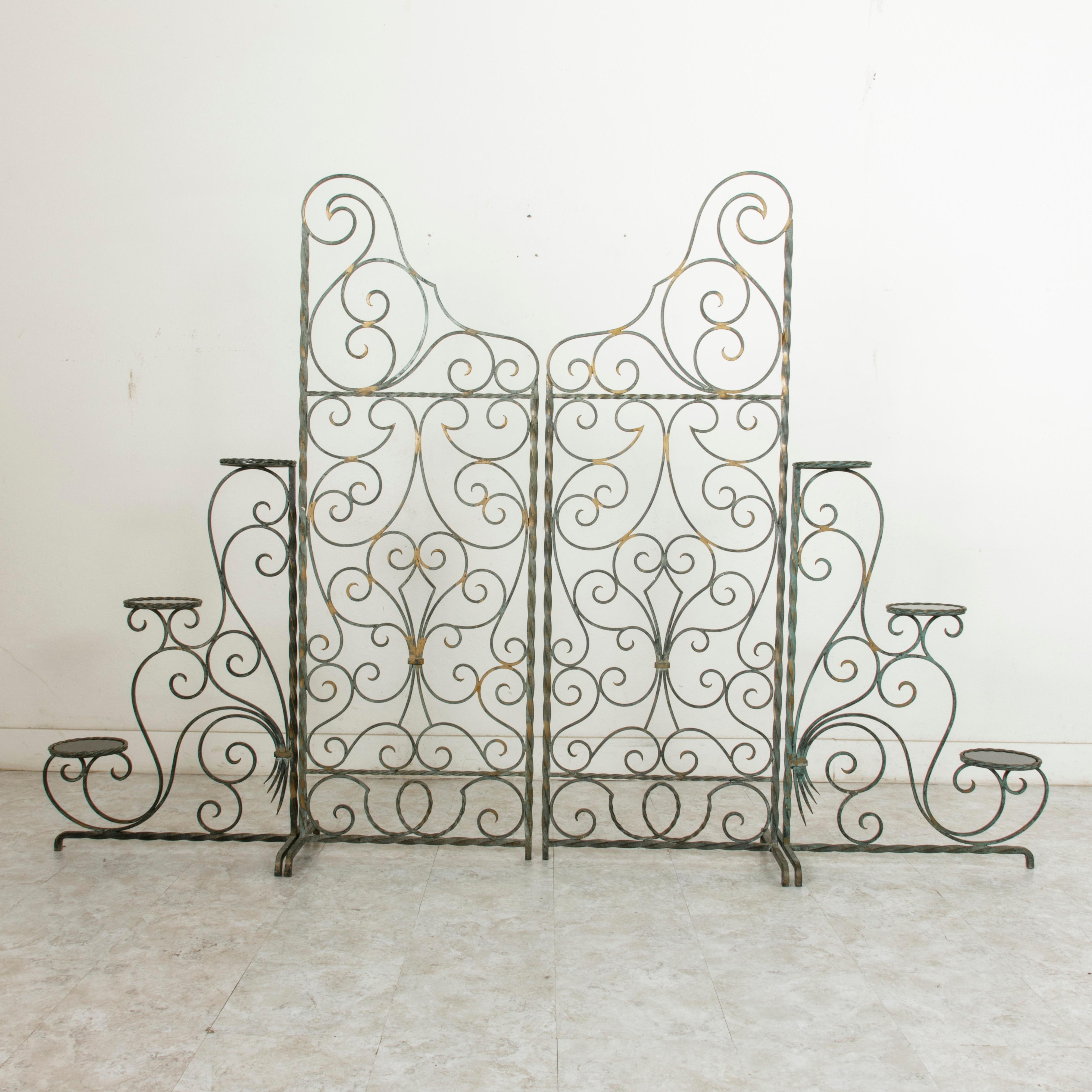 This set of four mid-20th century French wrought iron partitions features intricate scrolling ironwork with a green patina and hand painted gold detailing. The two taller sections each measure 68 inches high by 23.75 inches wide, with supports at