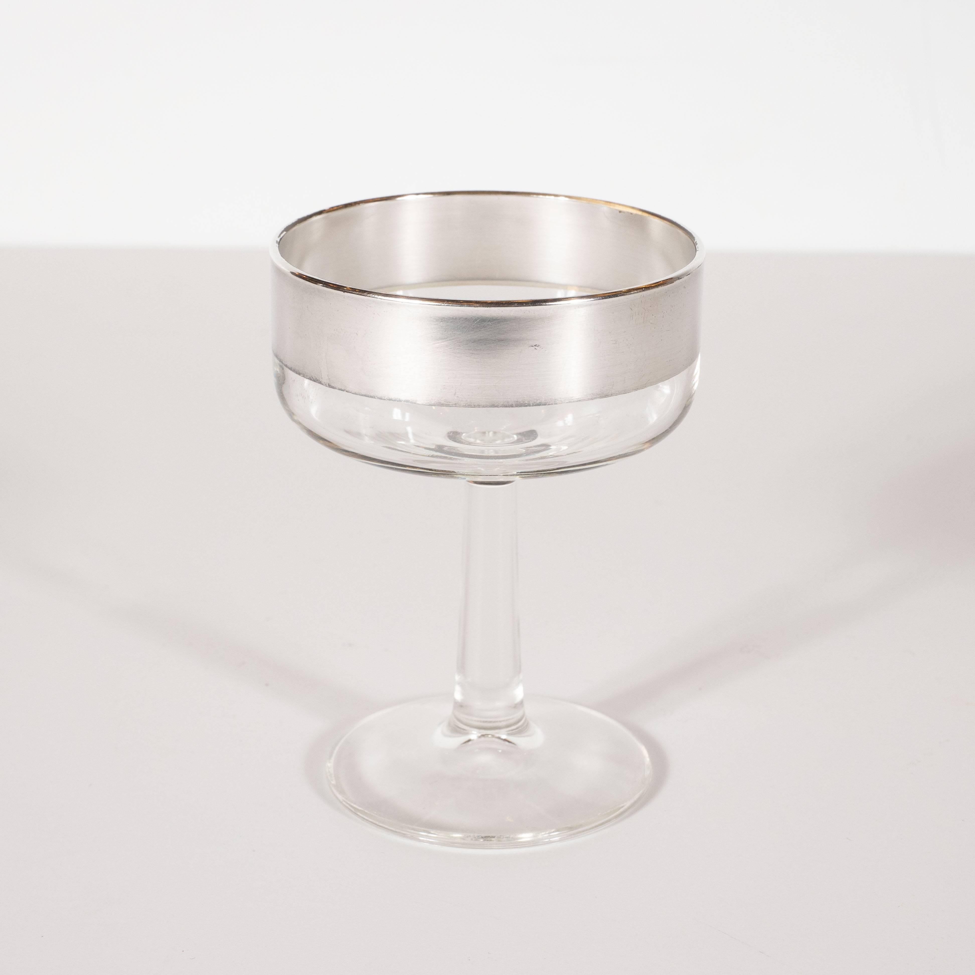 This refined set of four champagne coupes were designed in California by the esteemed Mid-Century Modern designer Dorothy Thorpe, circa 1950. Composed of simple cylindrical forms, they offer band detailing in sterling silver overlay at the top of