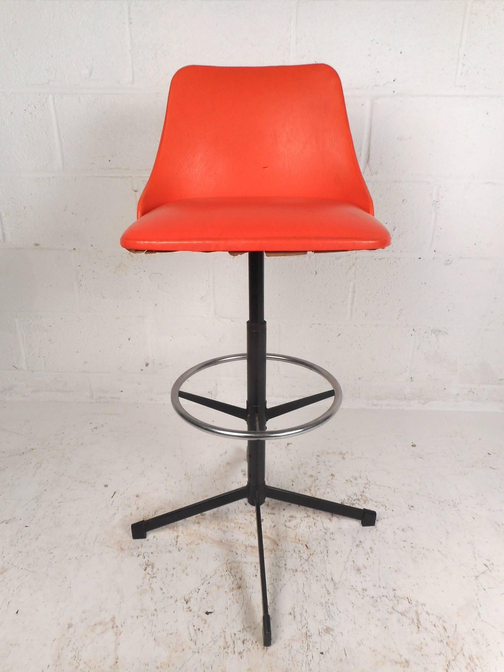 Stunning set of four vintage modern bar stools with orange vinyl covered seats and a sturdy metal base. Sleek design features a unique back rest with thick padded seats and a circular kick rest for convenience. The two-tone base and the splayed legs