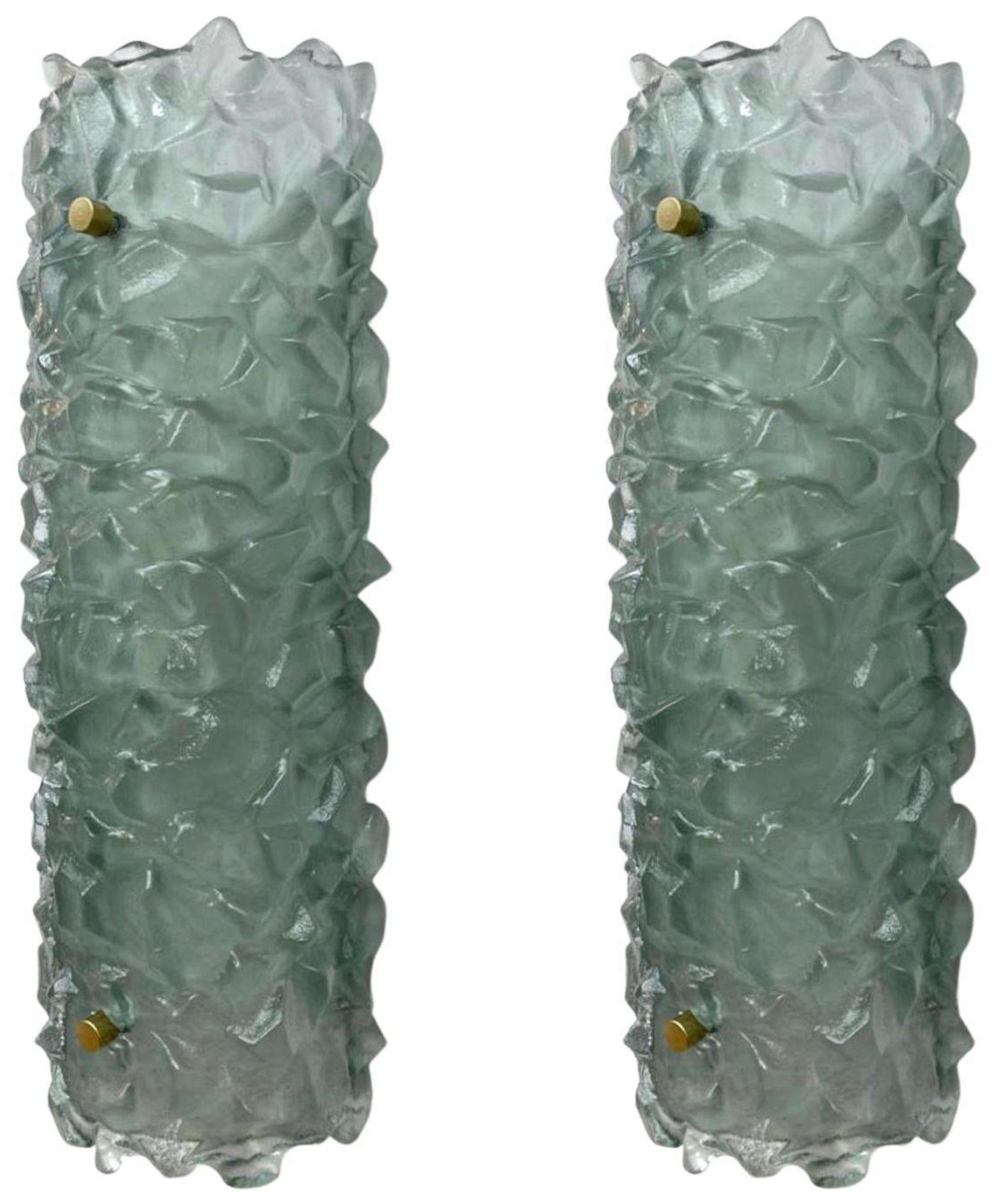 A striking set of four Italian modern wall sconces, each featuring a thick, hand-cast textured Murano glass shade in a subtle light green hue, mounted on minimalist white lacquered metal frames. The sculptural glass forms display a dynamic, organic