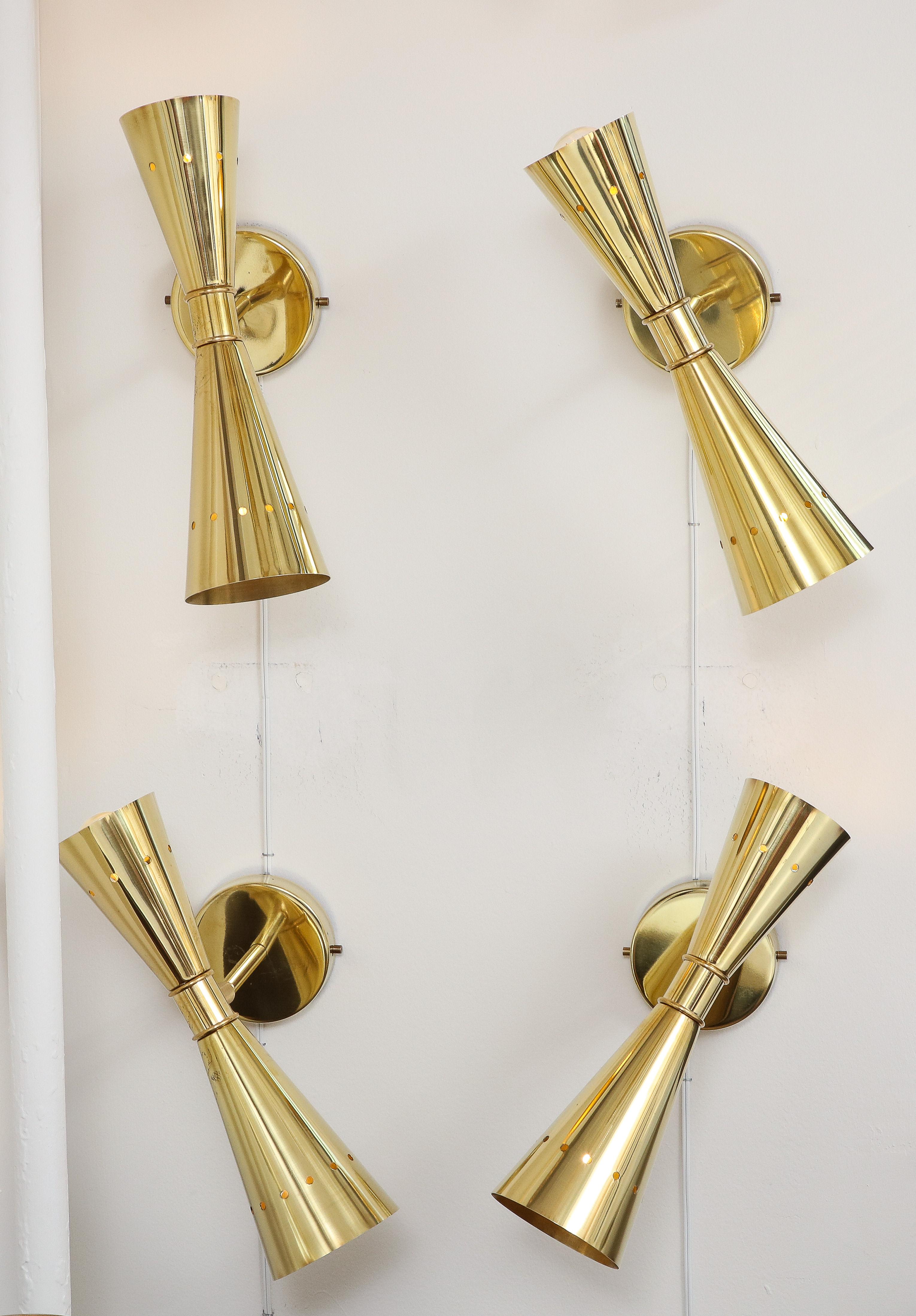 Set of Four (4) polished brass double cone (conical) swivel sconces, handmade in Italy. 
Two conical shaped brass structures, one large and one small, make up these modernist sconces.  Perforated details on cones allow light to pass through, giving