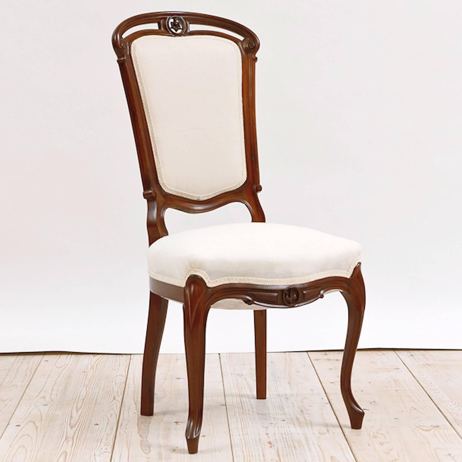 A very beautiful set of four Napoleon III dining chairs in mahogany with upholstered back and seat, cabriole front legs, and a carved lily on the arched and pierced crest rail, and on the apron, France, circa 1880. Chairs have been French-polished