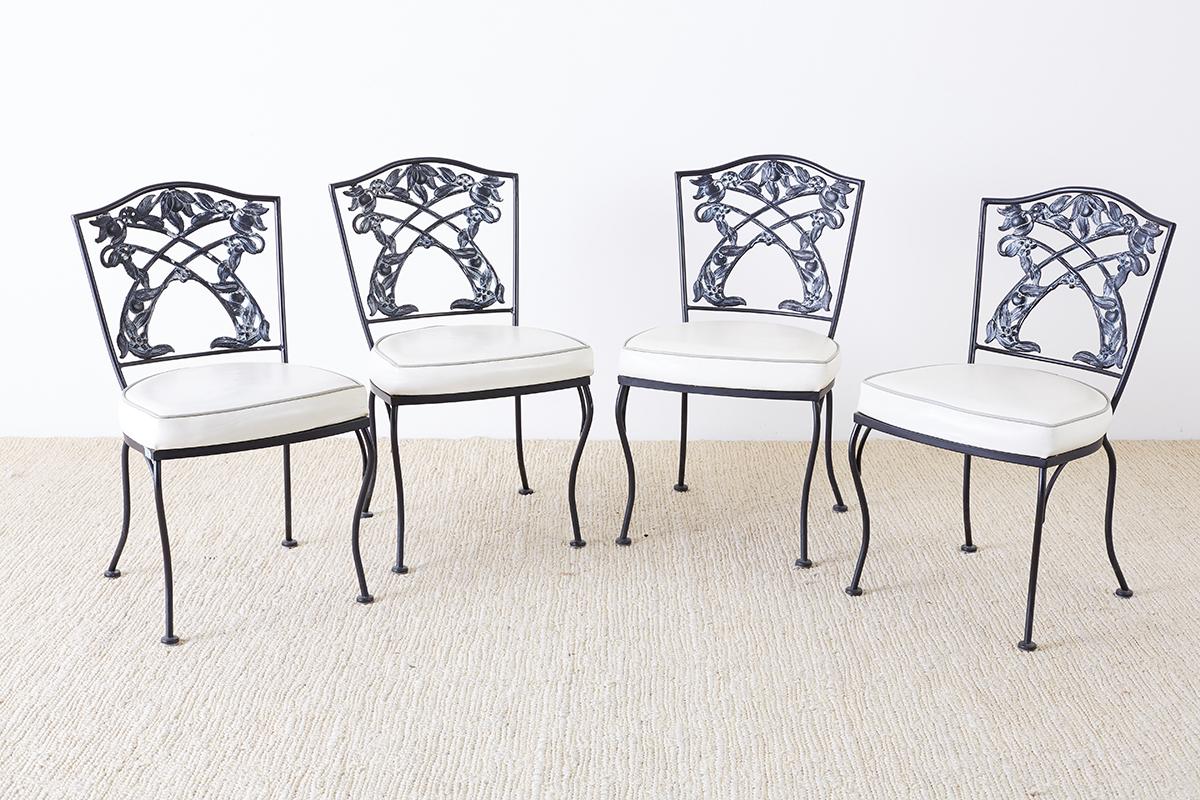 Mid-Century Modern set of four garden or patio chairs constructed from cast iron in the neoclassical taste. Featuring a decorative back splat with a fruit and foliate motif and humped crestrail. Light colored Naugahyde seats supported by round