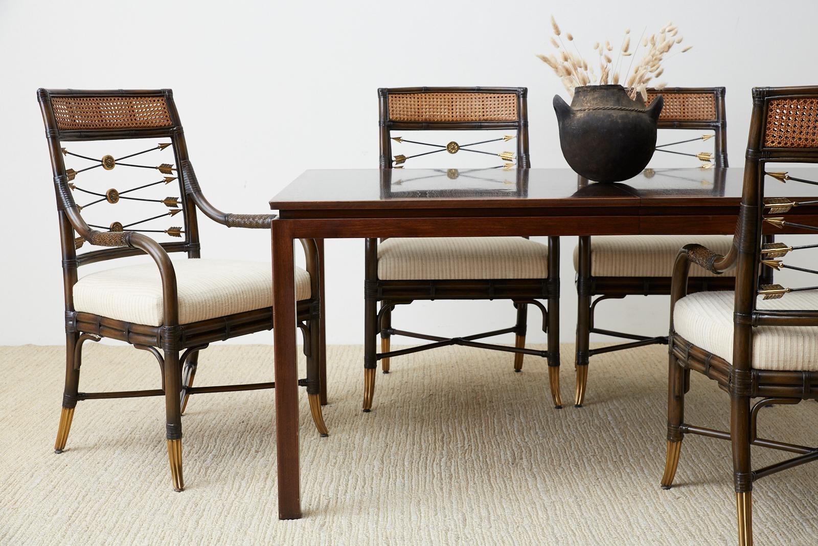 Amazing set of four bamboo rattan dining armchairs made in the style and manner of McGuire. The chairs feature neoclassical style bronze metal arrow motif backs. Each chair has three pairs of arrows centered by a bronze rosette medallion. The frames