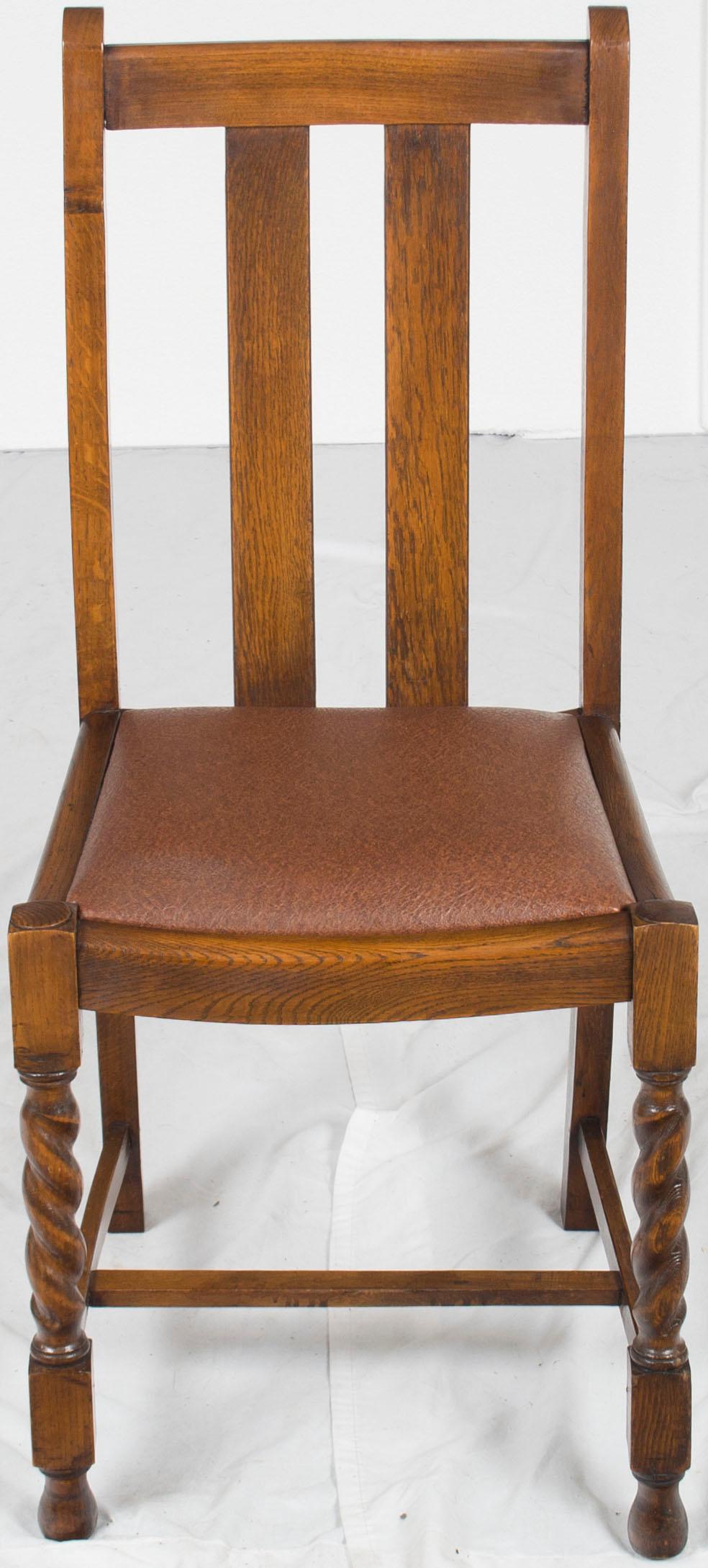 A traditional set of four English oak antique barley twist dining chairs. This set consists of 4 side chairs. All four were made with barley twist front legs and currently have brown leather upholstered seats. The upholstery looks fairly new with no