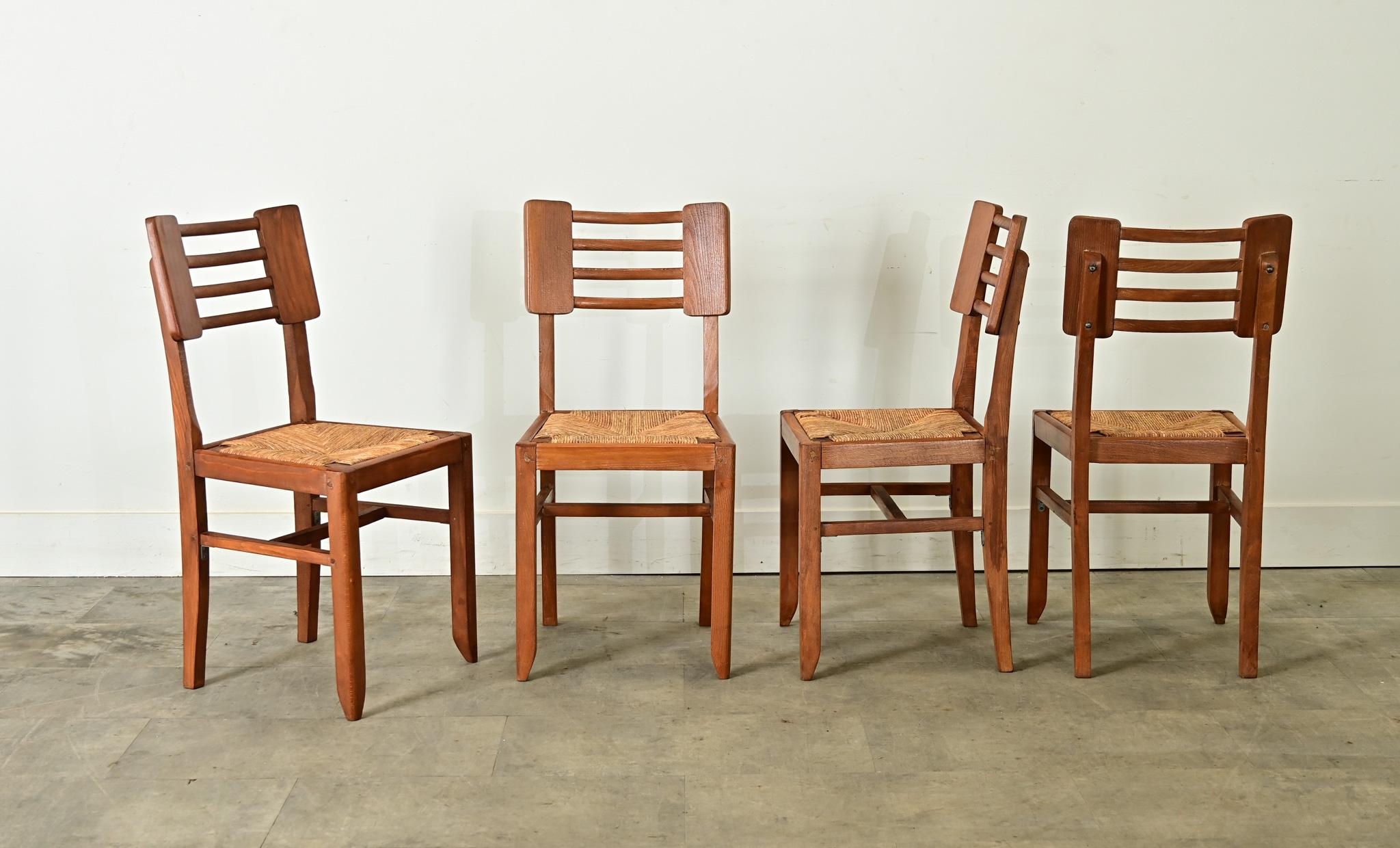 Midcentury modern set of four oak & rush seat chairs by designer Pierre Cruege, made in France, circa 1940s. The design features a lightweight but sturdy chair frame, consisting of wooden panels at the shoulder, connected by four slats supported by