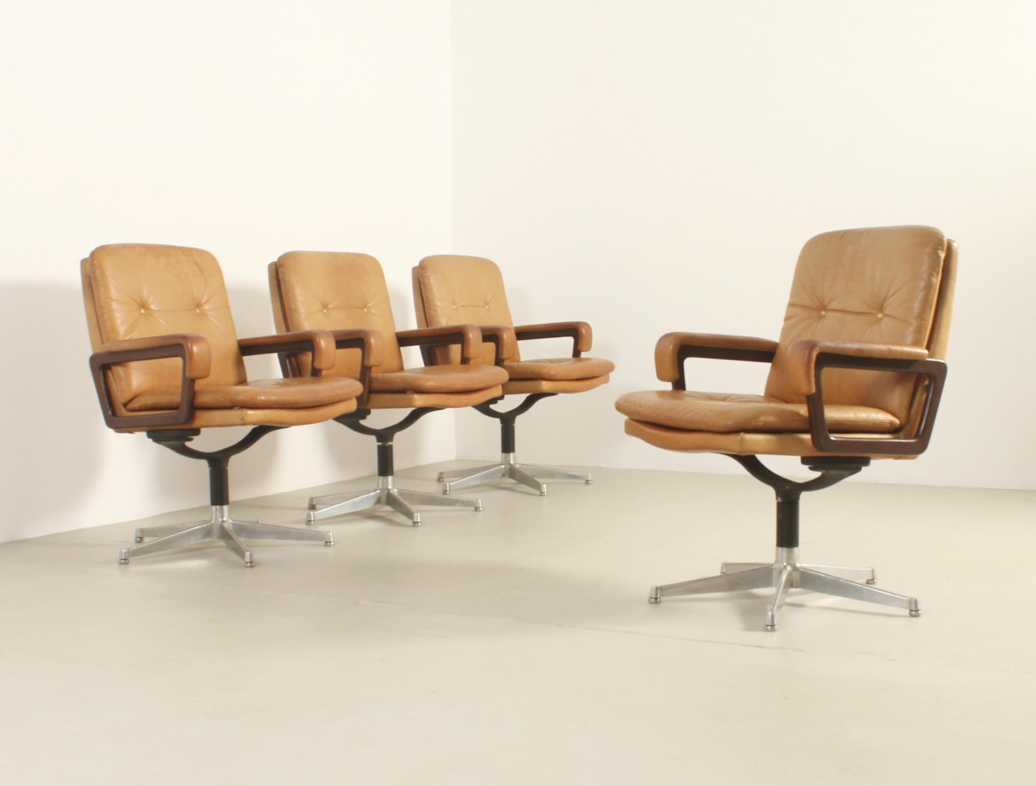 Set of four office armchairs designed by André Vandenbeuck in 1960's and produced by Arflex, Italy. Rare swivel desk version in original tan leather, wood arms and polished steel bases.