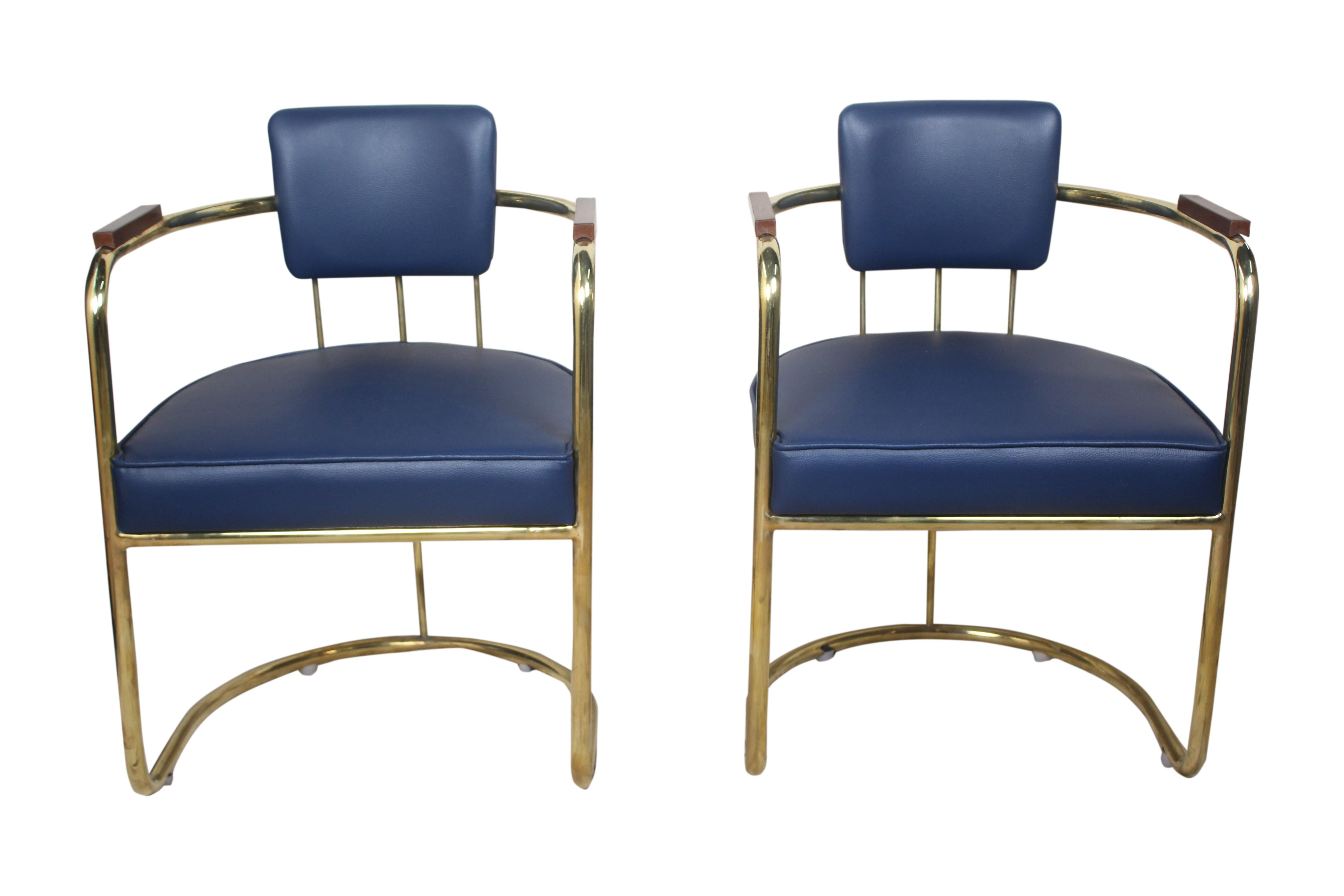 Pair of brass captain's chairs with teak armrests. Priced as a pair. Reupholstered navy blue cushions, late 1900s. From the salon of a cruising ship.