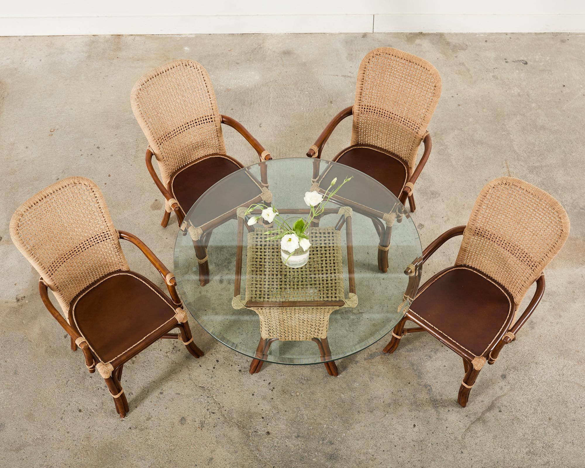 Suite da pranzo moderna e organica composta da quattro poltrone da pranzo in rattan e corda e un tavolo da pranzo con piano in vetro in rattan e corda. I telai in rattan sono legati insieme con una corda intrecciata. Il piedistallo del tavolo è