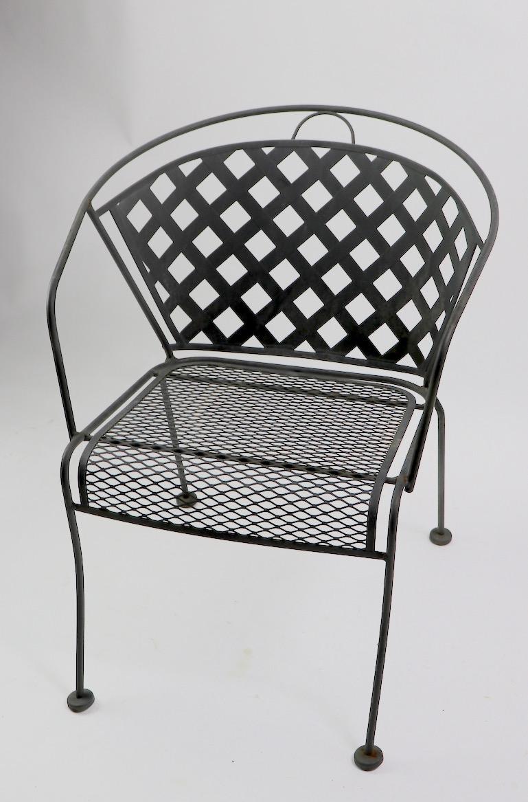 Set of four wrought iron and metal mesh dining height armchairs attributed to Woodard Furniture Company. Each chair has a wrought iron frame, metal mesh seat and larger weave pattern mesh back. All four are in very good original condition showing