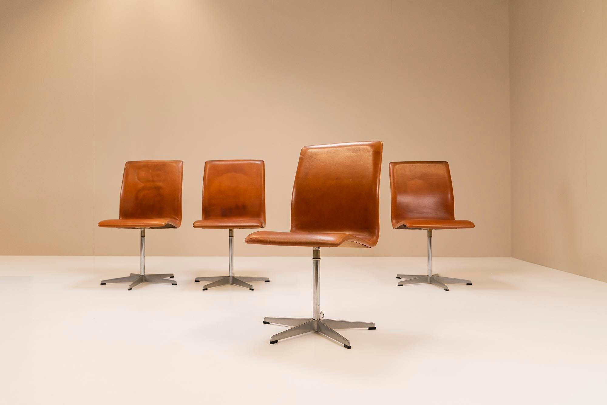 Satz von vier 'Oxford Chairs' Esstisch-Drehstühlen mit brauner Lederpolsterung und Metallgestell. Diese Stühle mit dem Modell 3171 wurden 1965 entworfen und zu einem späteren Zeitpunkt von Fritz Hansen ausgeführt. Die Stühle haben eine schöne Patina