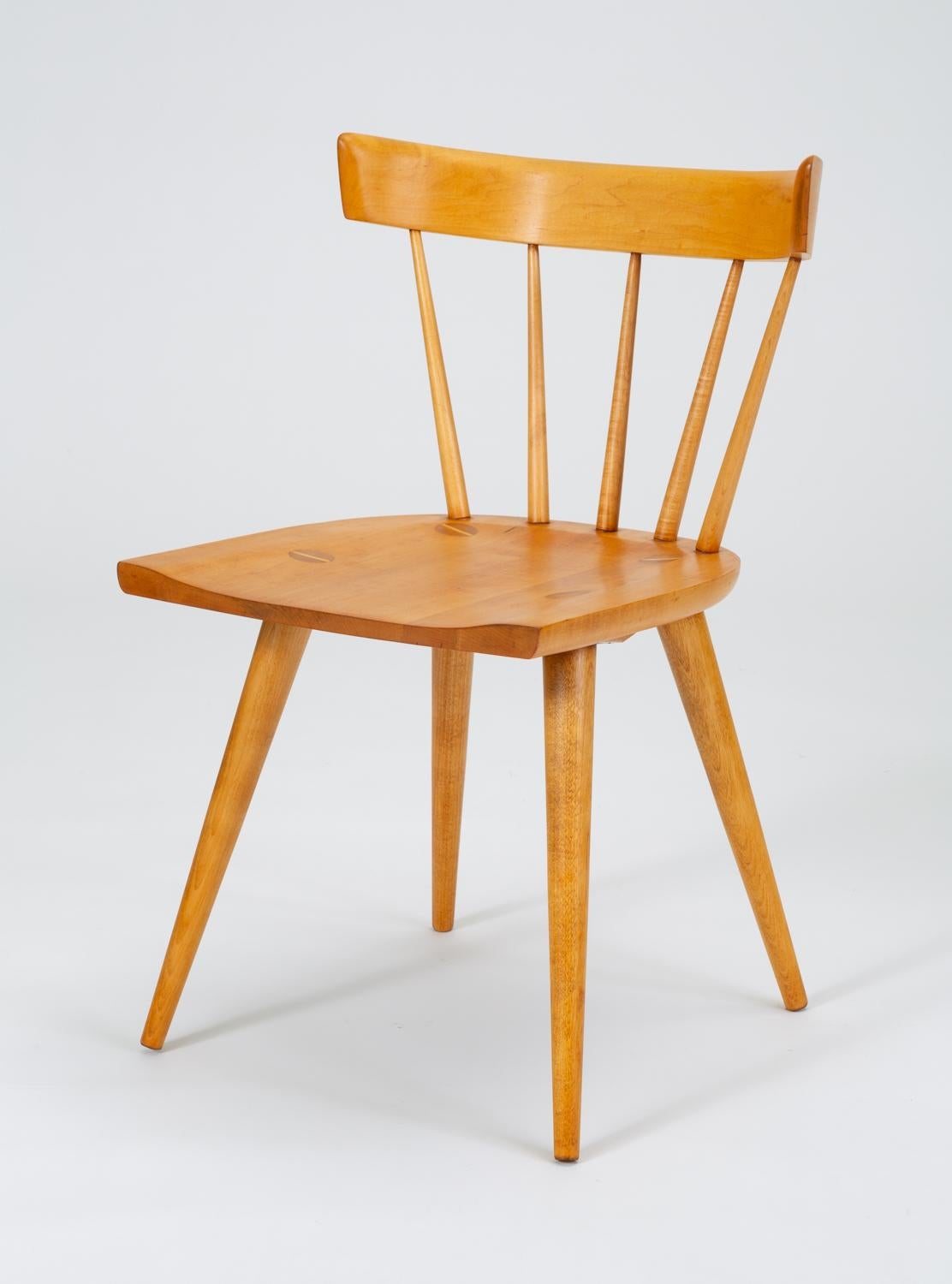 A set of four dining chairs in solid maple from Paul McCobb's iconic Planner Group, manufactured from 1950-1964 by Winchendon Furniture. The chair, model #1531, takes its basic inspiration from a Windsor chair, with a low spindle back of tapered