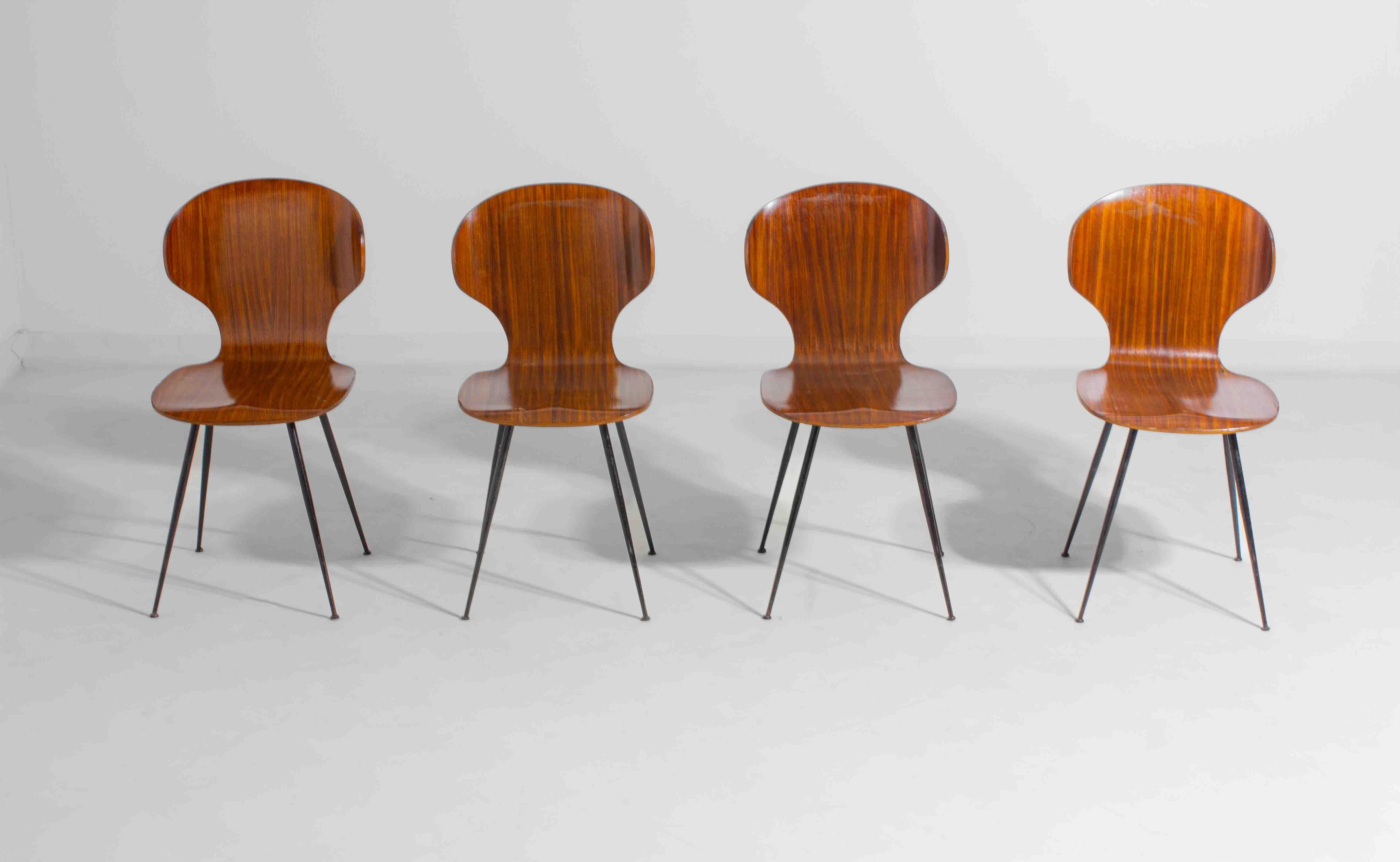 Elegant set of four ‘Lulli’ chairs designed by Italian architect Carlo Ratti in the 1950s for Industria Legni Curvati Lissoni. The curved plywood seat and backrest are shaped in one continuous form and rest on slender black metal legs. The rich wood