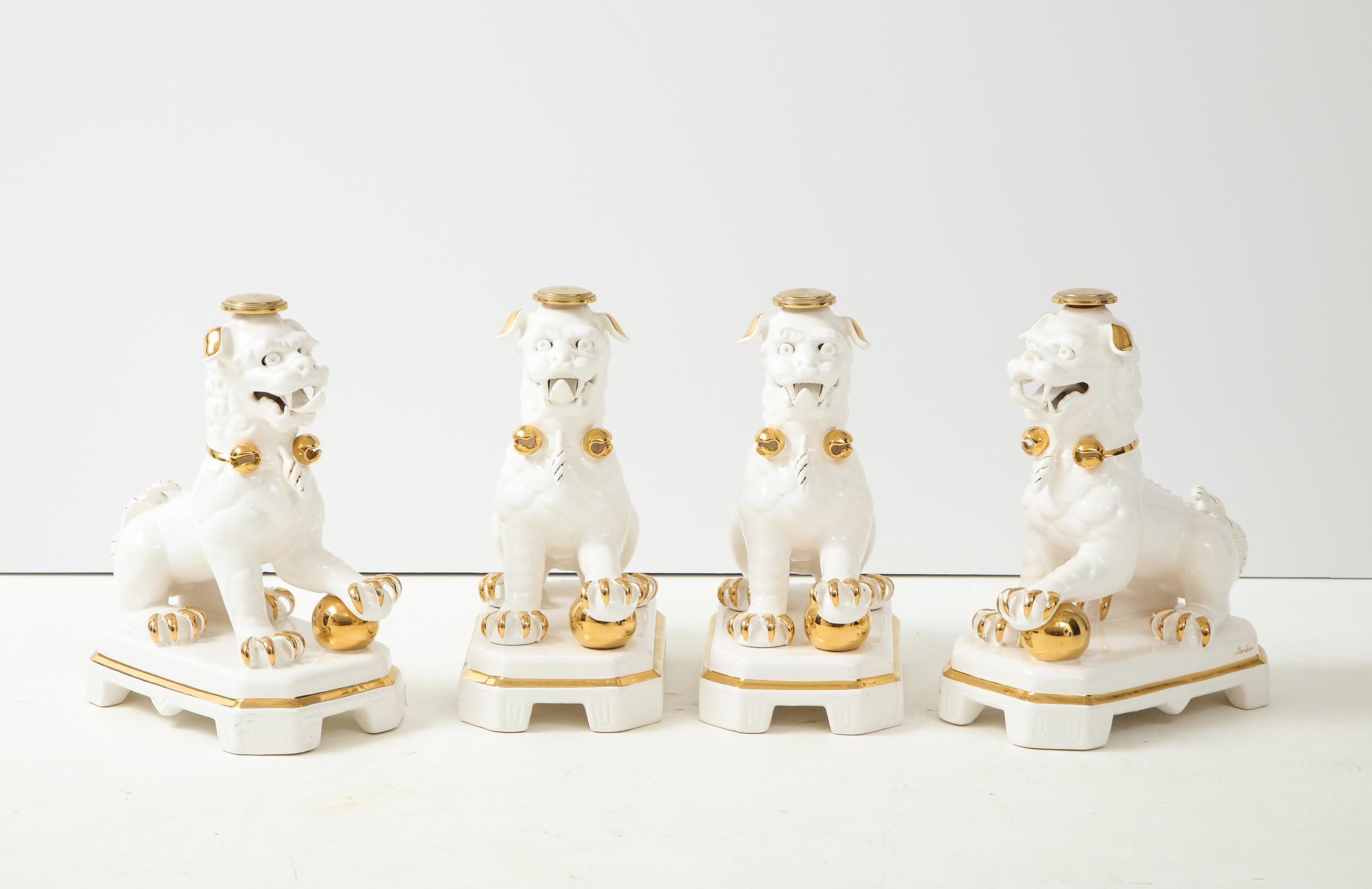 A set of four white and gold ceramic Foo Dog table bases. Made in Spain by Bondia in the Hollywood Regency style. Ornate ceramic sculptures with detailed faces, mouths, bodies, and paws. All four Foo Dogs are male with a front paw on a ball. Each of