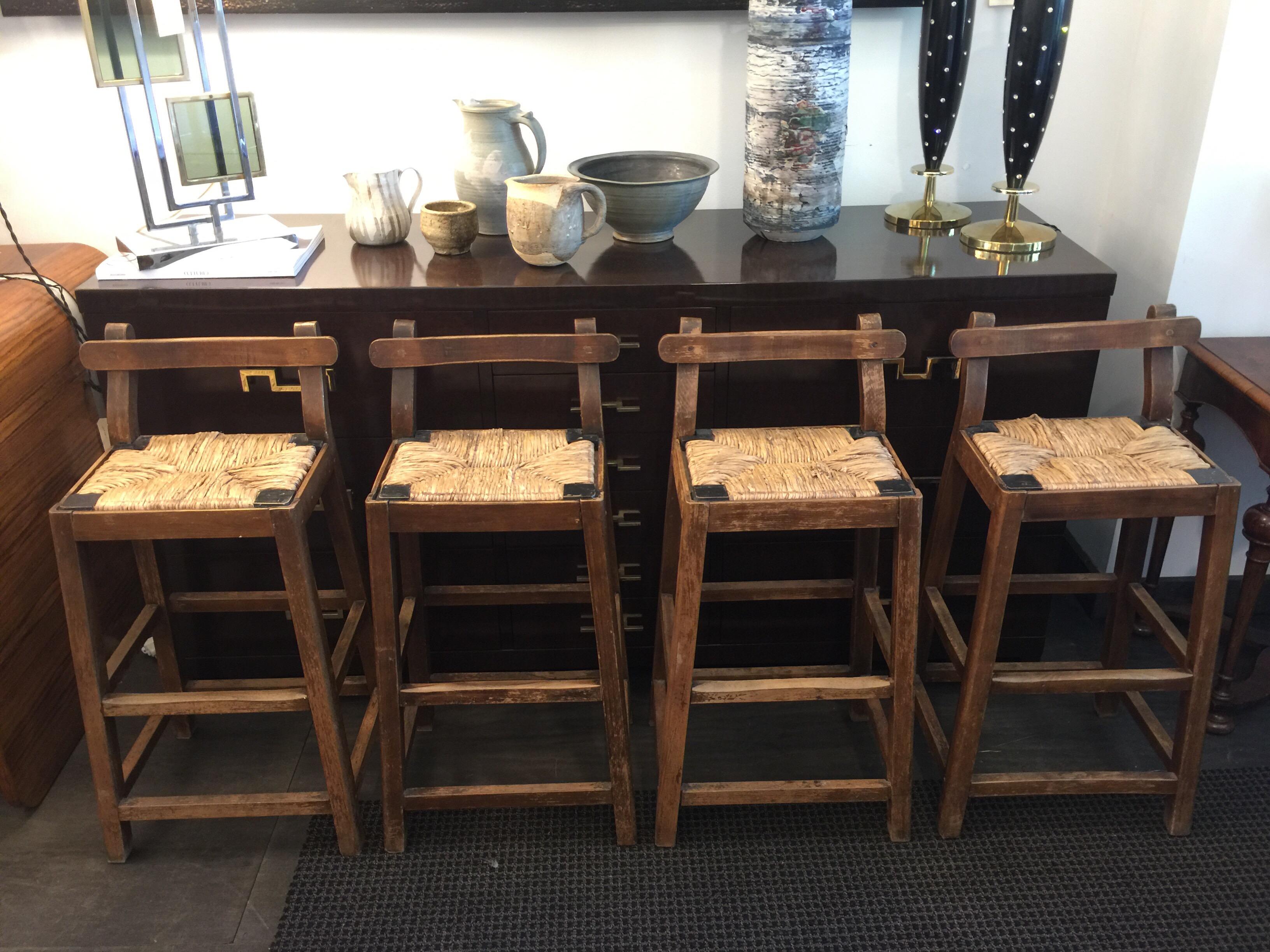 These are small in scale bar stools, more like accent seating. Beautiful wear and distress on these primitive style items. Seats are woven rush - all in nice original condition. Very sturdy for their size and desirable for a rustic environment.