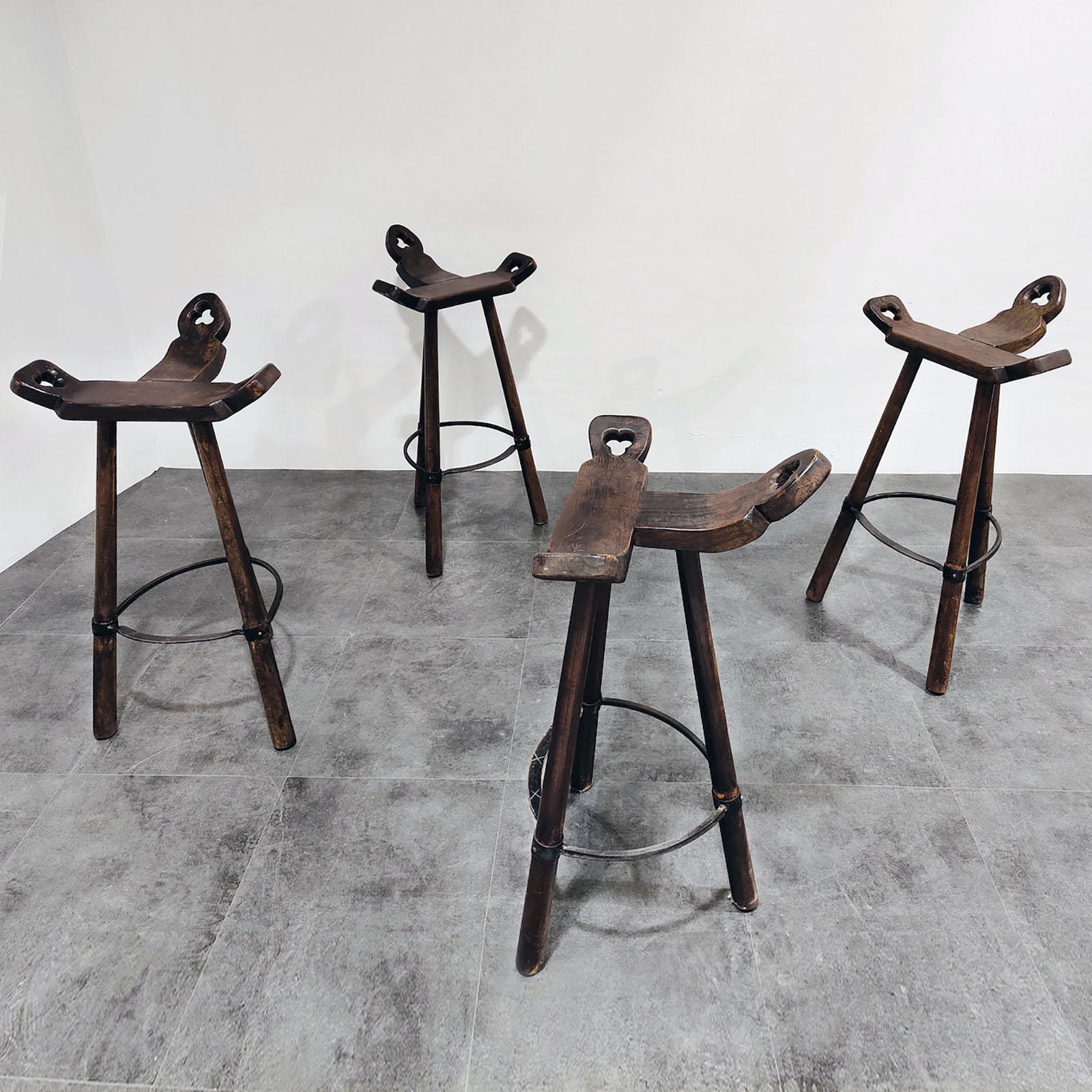 Handsome set of four tripod bar stools with hand-wrought iron footrest.
Four Marbella bar stools in stained oak wood and with a metal ring in the style of Sergio Rodrigues. The curved T-shape seat makes the seating very comfortable. The three