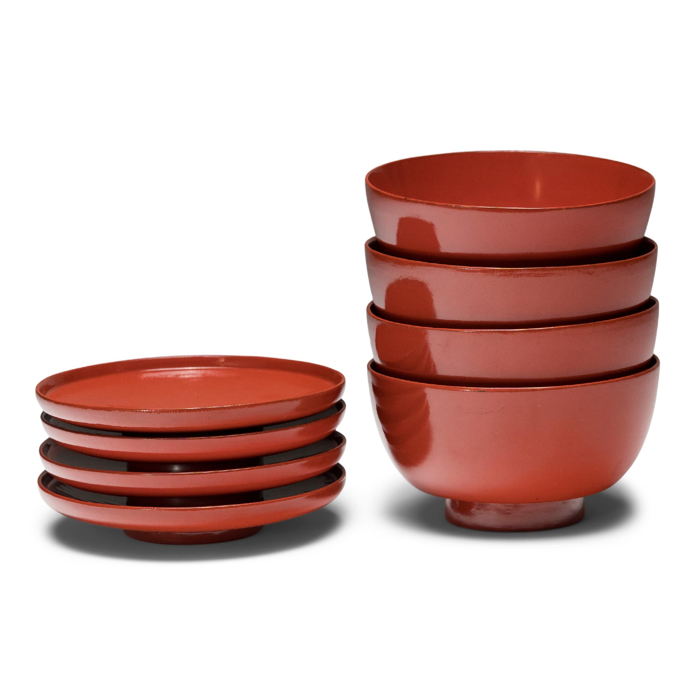 This set of four lacquered rice bowls is simply shaped with gently tapered sides and a footed base, accompanied by matching footed lids. A rich, glossy red finish coats the bowls and lids inside and out, with a contrasting black lacquer detailing on