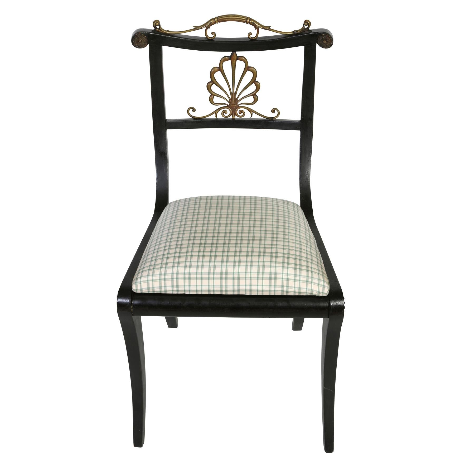 A vintage set of four ebony Regency style dining chairs with newly upholstered silk check cushions in blue on a cream background.  The four chairs have brass details on the chair crest and back with a brass shell and swirl motif.  A traditional set