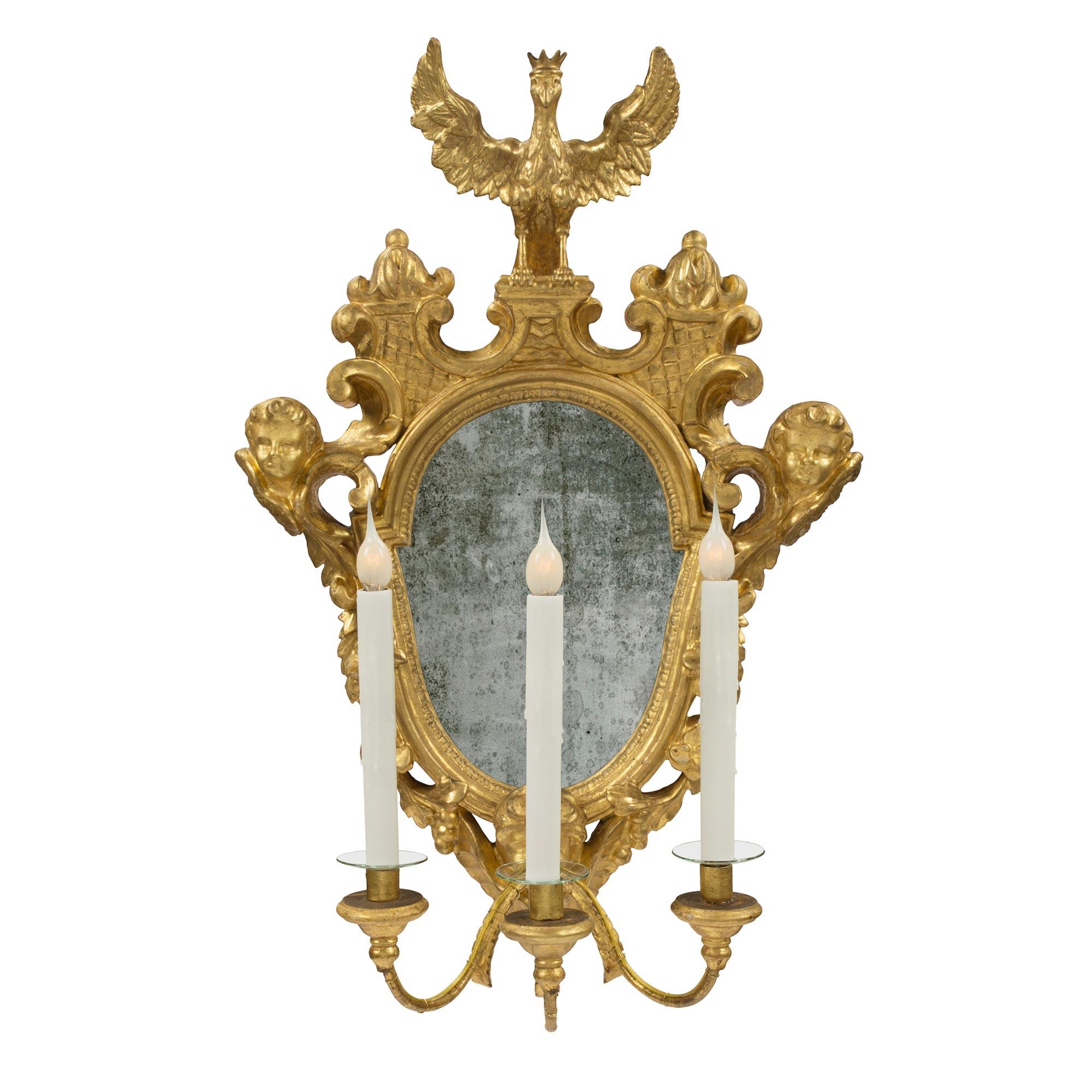 A spectacular, extremely high quality and unique set of four Roman 18th century giltwood electrified mirrored sconces. At the bottom of each mirror, three S scrolled arms protrude from the charming face of a cherub. Each arm is decorated with