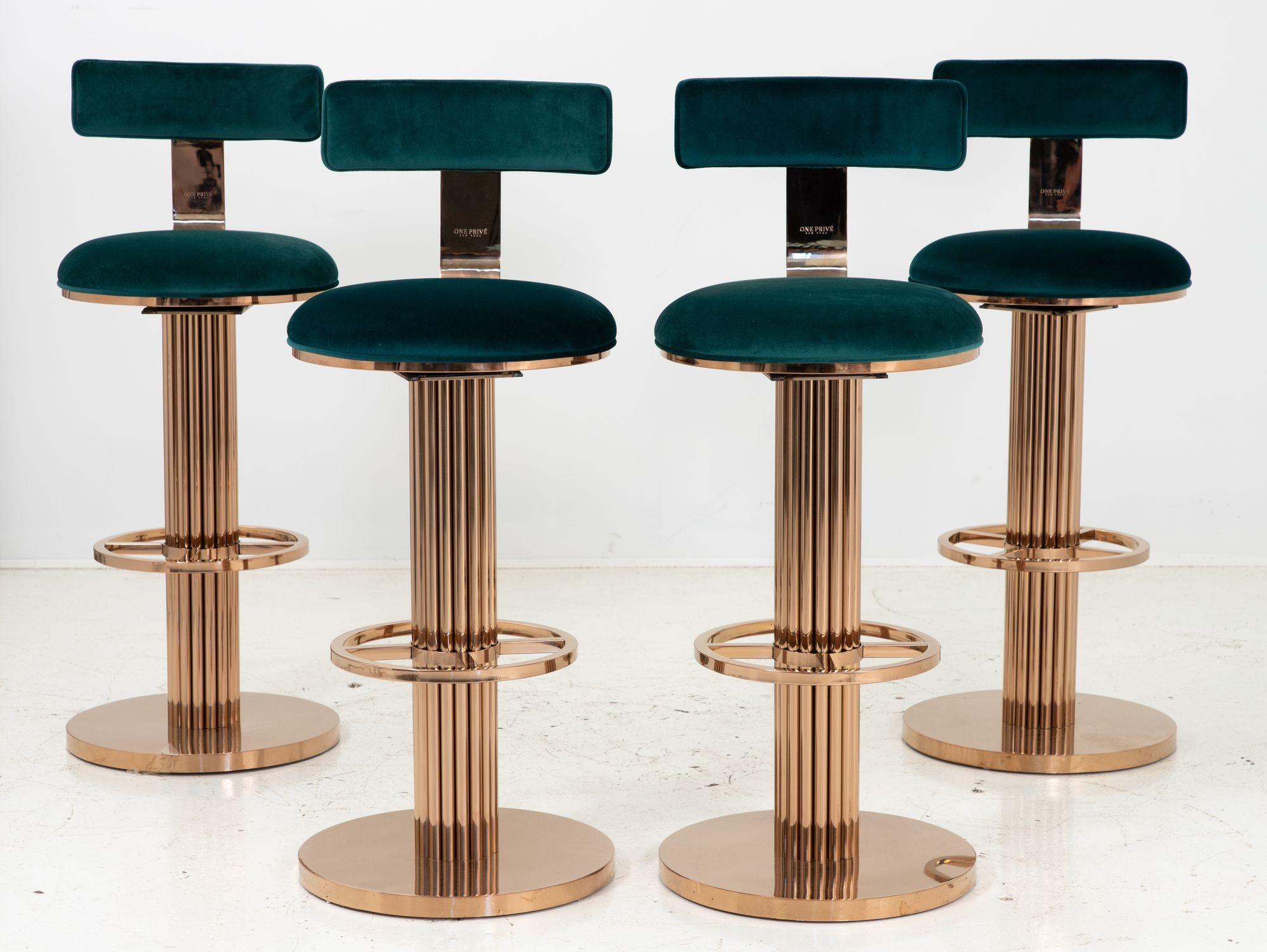 A set of four barstools with a subtle rose gold finish and emerald velvet upholstery. This set is a reproduction of the Art Deco style Design For Leisure stools that were produced in the 1980s. Each base has a fluted design with a foot rest.