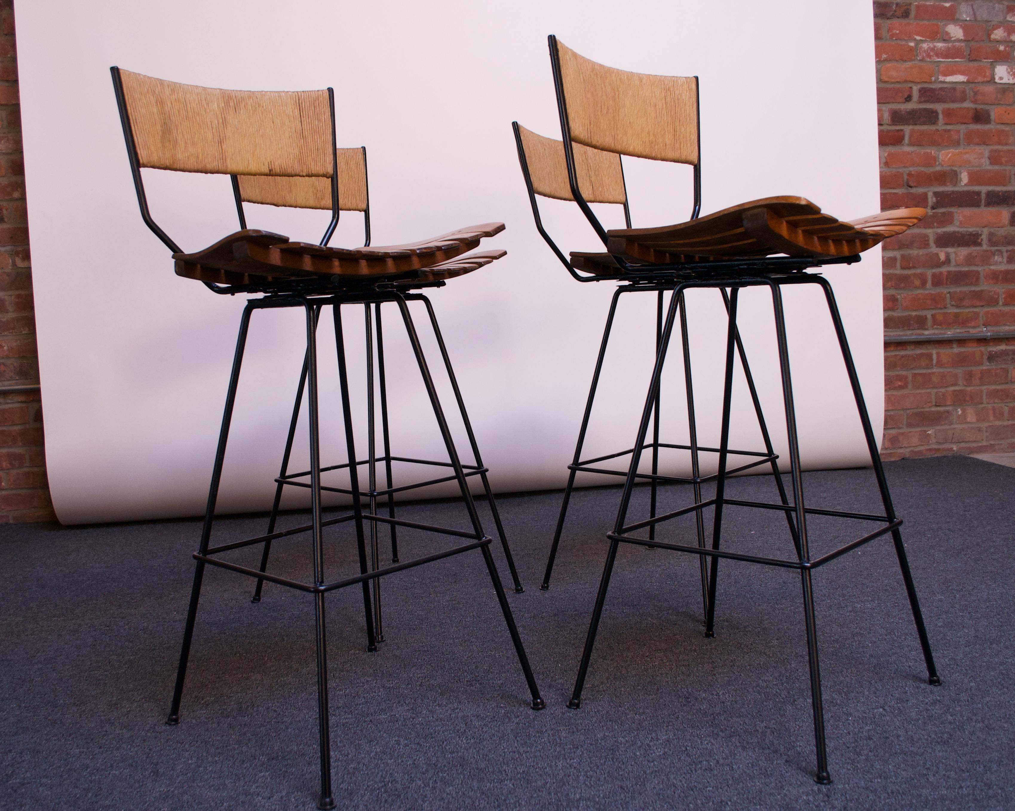 Set of four Arthur Umanoff for Shaver Howard bar stools composed of wrought iron frames with stained birch-slatted seats. Modernist, rectangular rush back adds a striking contrast to an otherwise modest form. Swivel seat allows for full 360 degree