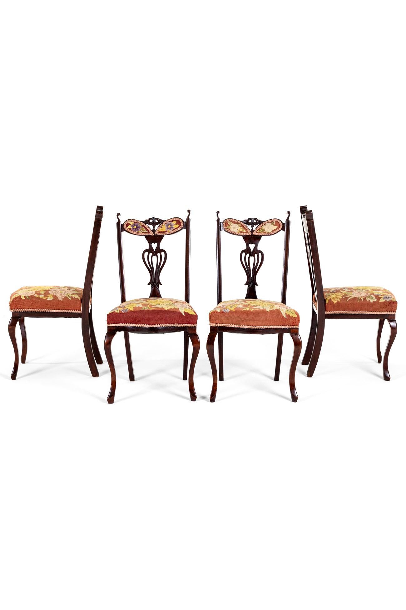 A set of four Victorian mahogany dining chairs with fine embroidery work floral seat cushions and back rests.

The chairs exhibit a shaped cresting rail with carved ears over a Chippendale style splat, pierced and carved with scrolls and