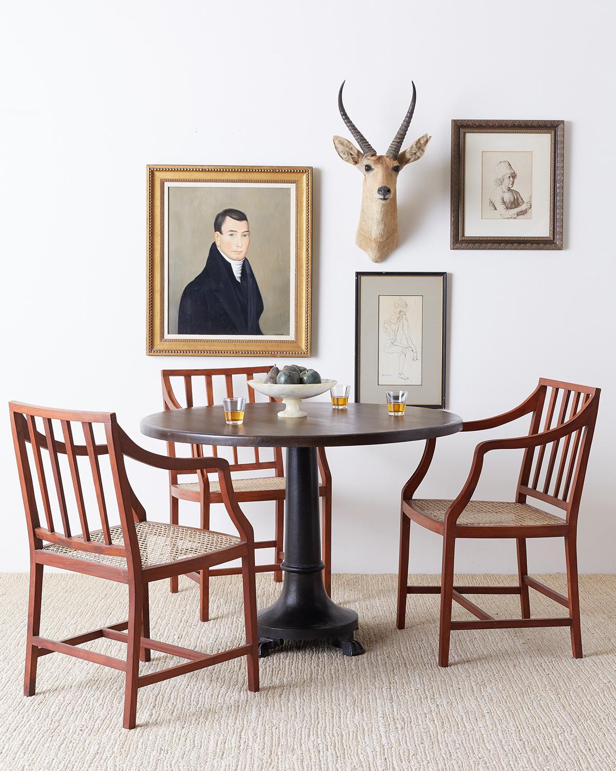 Stylish set of four slat back hand carved dining chairs featuring a hand-caned seat. Each chair has long, graceful finger carved arms and is supported by elegant square legs with H shaped stretchers. Understated with a warm teak finish and excellent