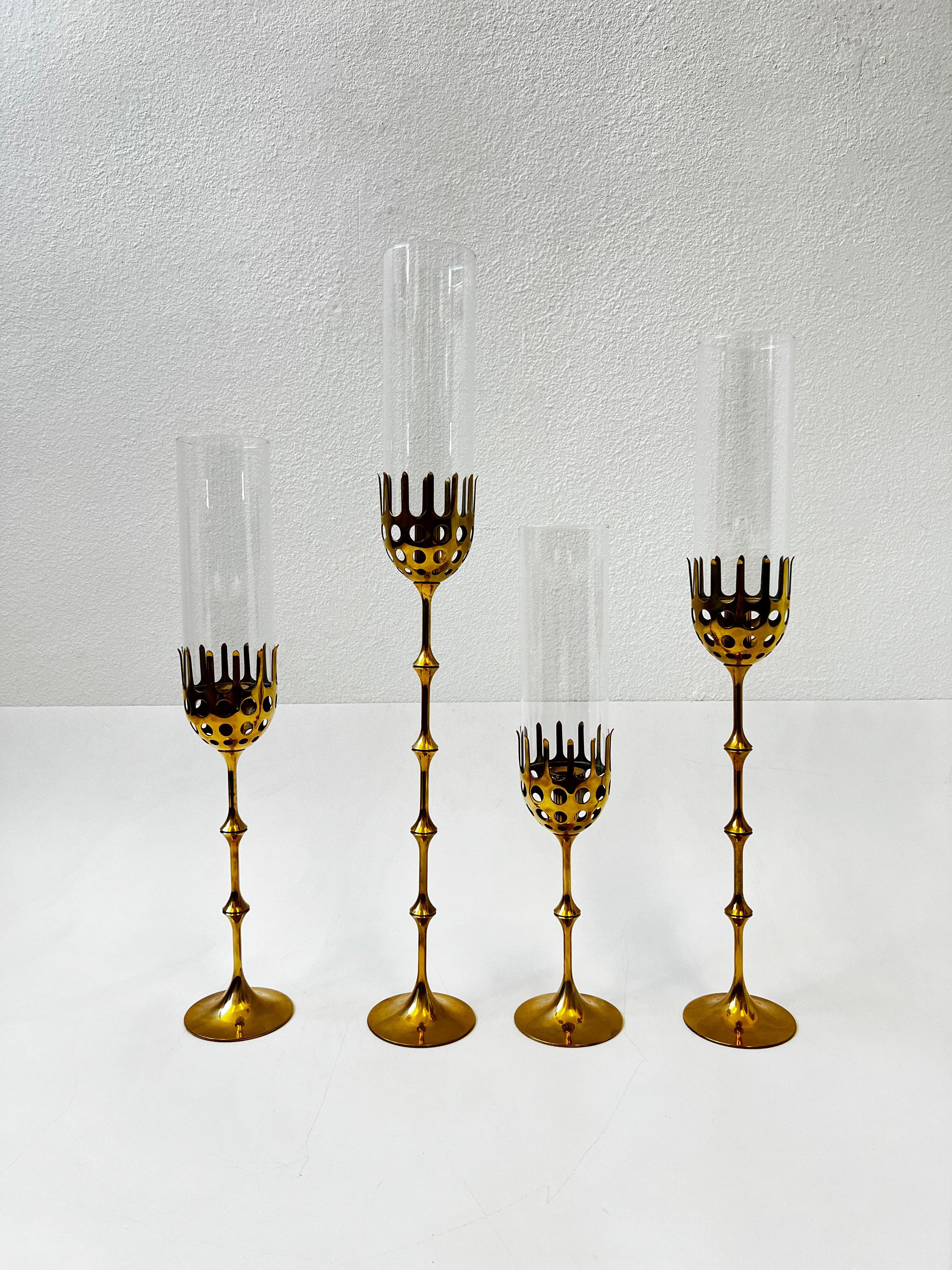 Beautiful set of four hurricane candle holders designed by renowned Danish designer Bijorn Wiinblad. 
Constructed of solid brass and glass. In original vintage condition, they show minor wear consistent with age. 
The brass is not lacquered. They