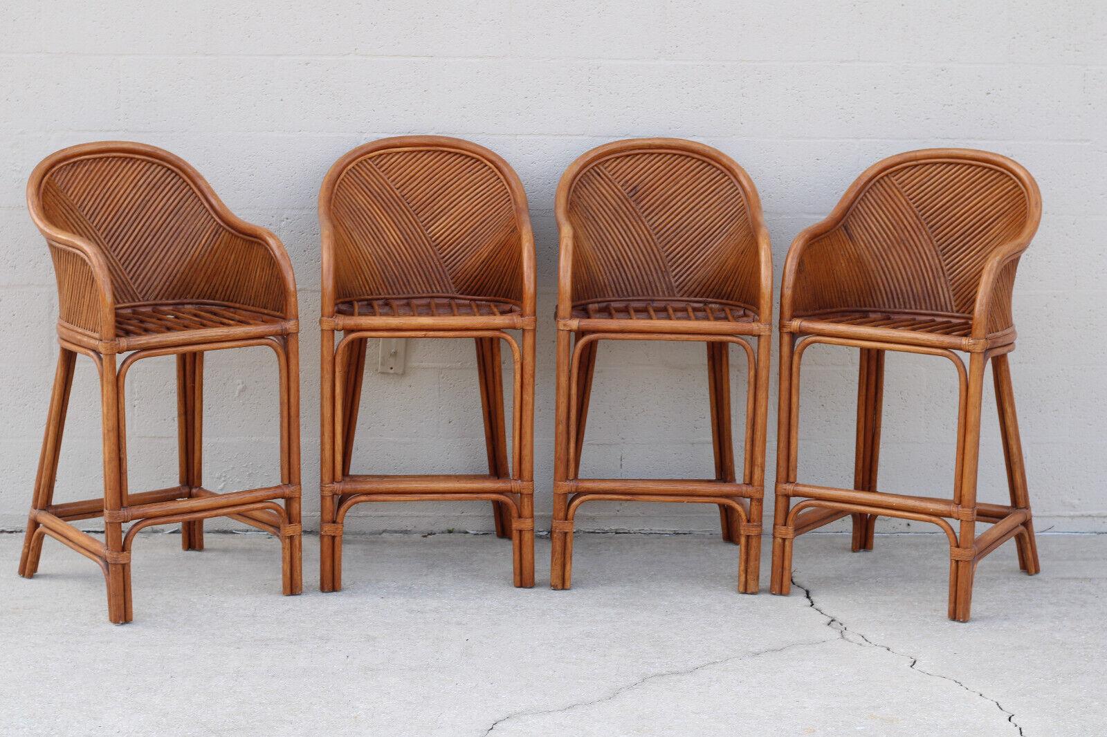 Vintage set of four sculptural pencil reed rattan bar stools. Stools have a rattan frame and feature a barrel-back design, a stick deck, and leather bindings. Hand-crafted and of solid construction, the bar stools are finished in a rich tobacco