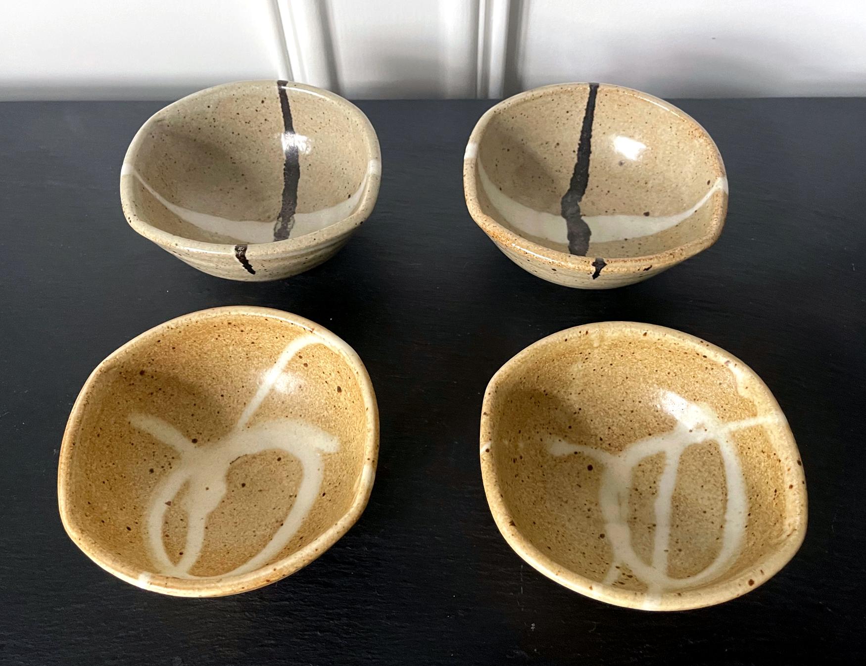 Un ensemble de quatre bols à thé en grès du céramiste américain Warren Mackenzie (1924-2018). Les bols ont été empotés à main levée avec une forme circulaire légèrement irrégulière. Présentés en deux paires, la surface des bols a été recouverte
