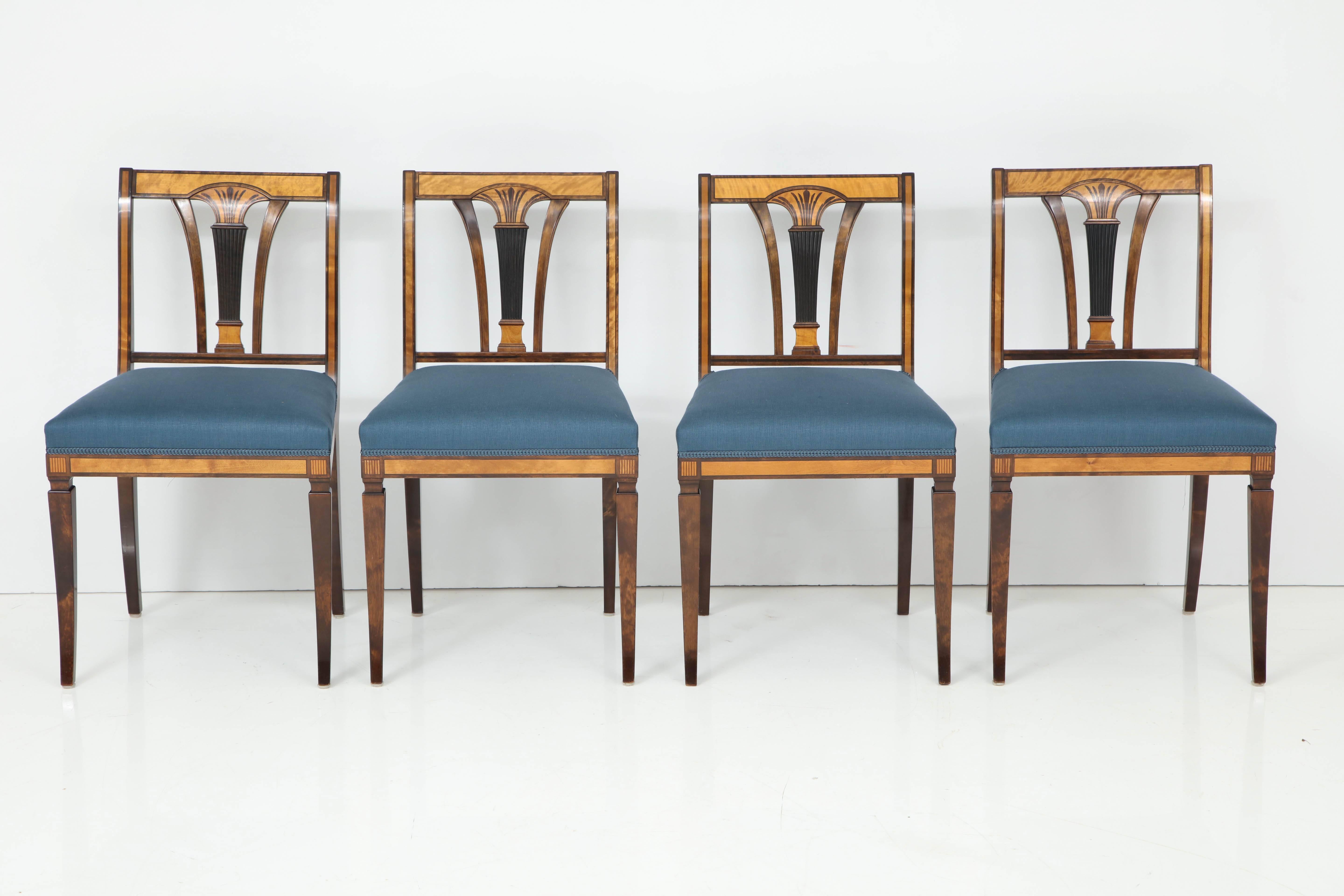 A set of four Swedish Grace birch, fruitwood and stencil decorated side chairs, circa 1930s, each with a rectangular backrest with a carved and decorated classically inspired back splat, upholstered seats raised on sabre legs.