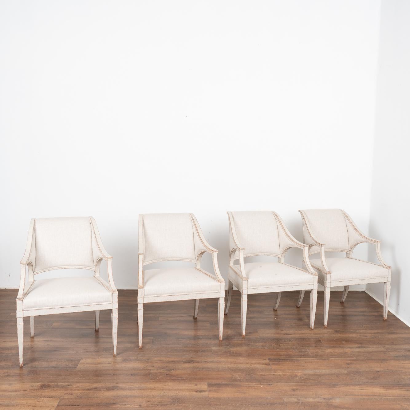 Set of four, sleek and stylish Gustavian Swedish arm chairs with sabre back legs. 
Simple linen upholstery on seat, back and arm sides.
Restored, later professionally painted in layered shades of white and lightly distressed to fit the age and grace