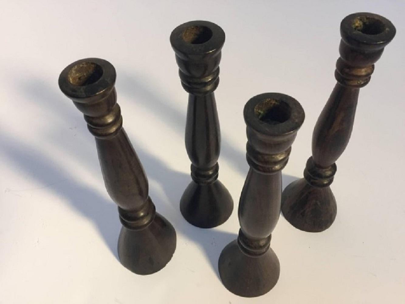 A sculptural set of four candlesticks hand-turned in ebonized wood, each in an elongated form, two slightly shorter than the other. Midcentury hand-carved heavy candlestick made in India for the British market.Dimensions: 11.5 in. H x 3.25 in. D.