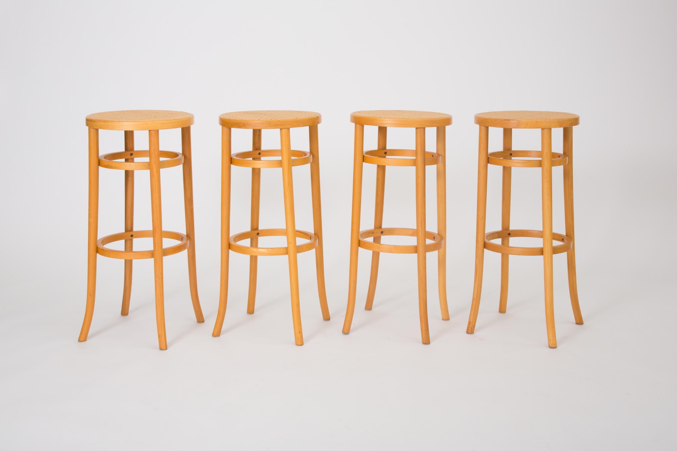 A set of four 1980s American-made Thonet Industries round bar-height stools, manufactured in Thonet’s signature bent birchwood with woven cane seats. Each stool has four rounded saber legs and two support rings below the seat and at foot level. The